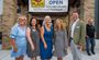 Five professionals are pictured in front of the new doors of Bentonville My Place, with a now open sign hanging above them.