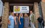Five professionals are pictured in front of the new doors of Bentonville My Place, with a now open sign hanging above them.