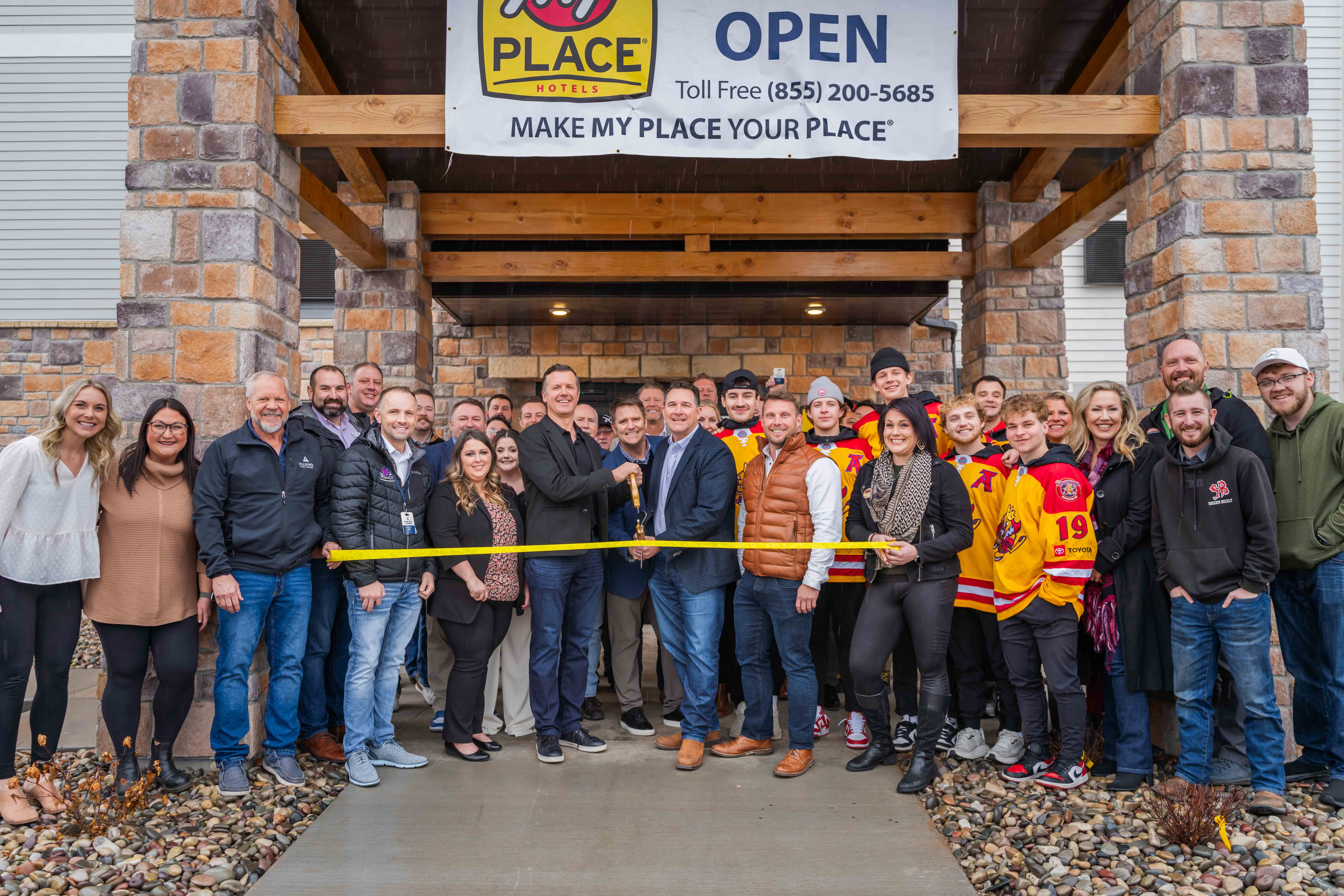 A group of people posing outside of My Place Hotel for a ribbon cutting photo