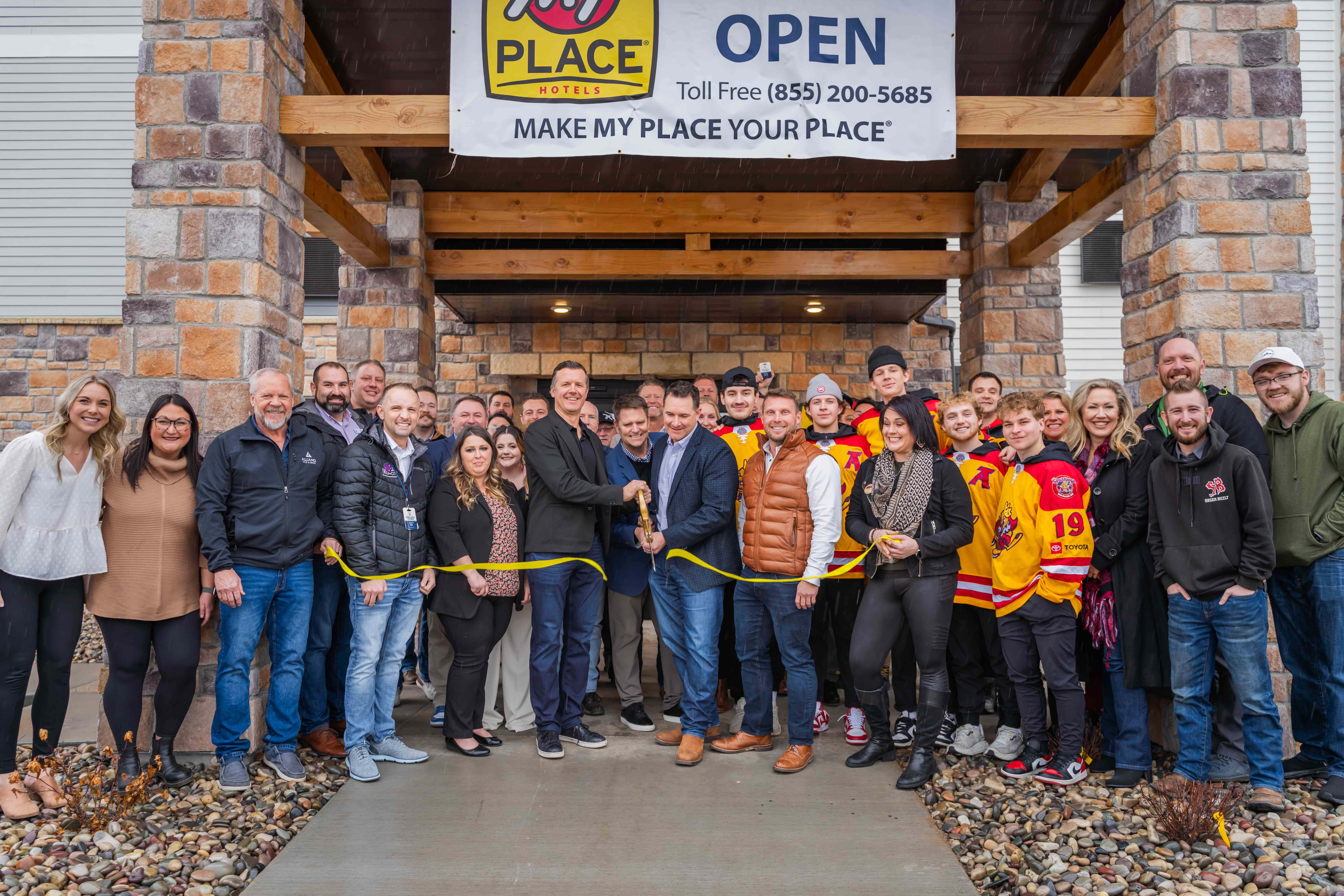 A group of people posing outside of My Place Hotel for a ribbon cutting photo