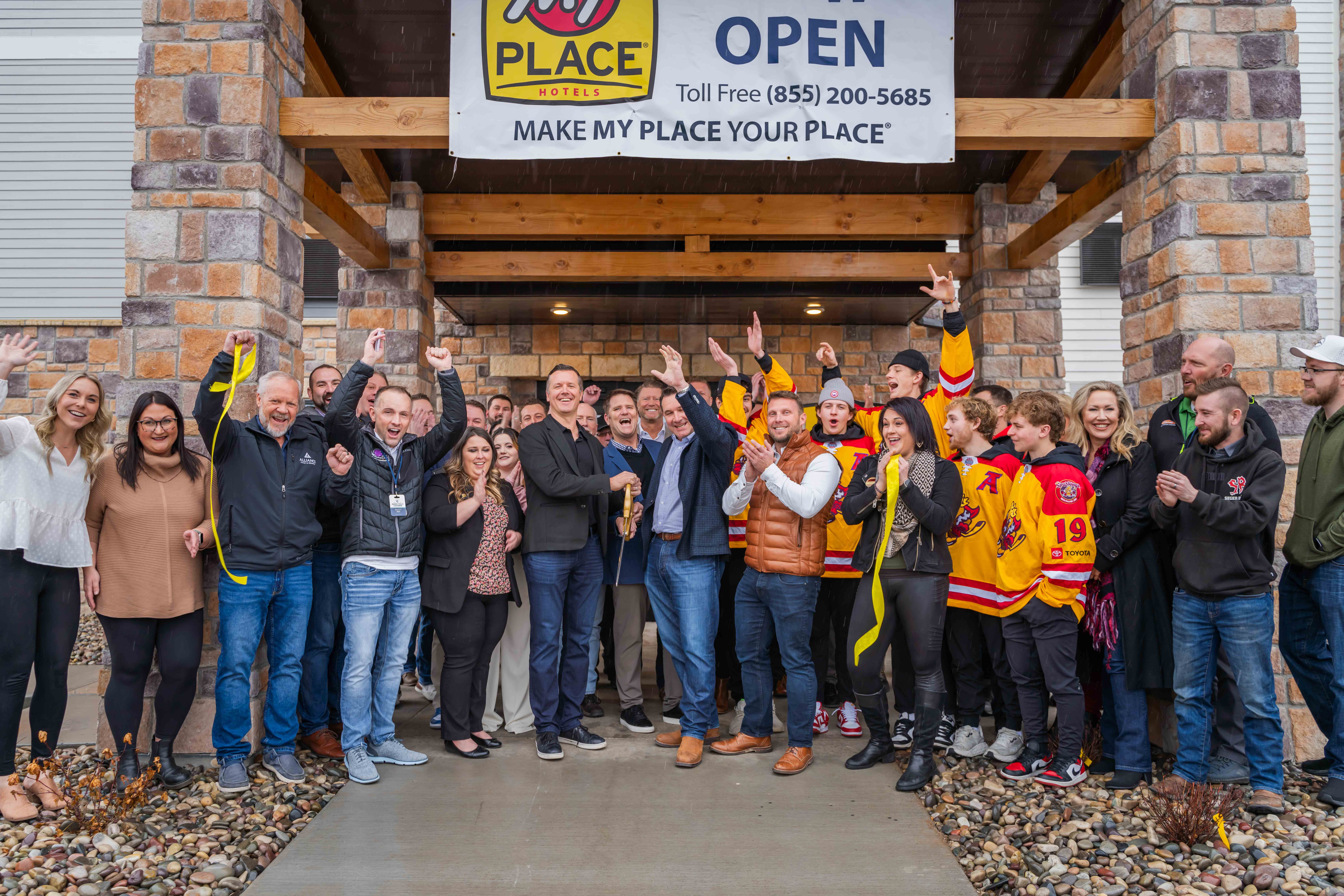 A group of people celebrating outside of My Place Hotel during a ribbon cutting