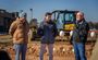 Three professionals are pictured in conversations, standing in front of a tractor used for the groundbreaking.