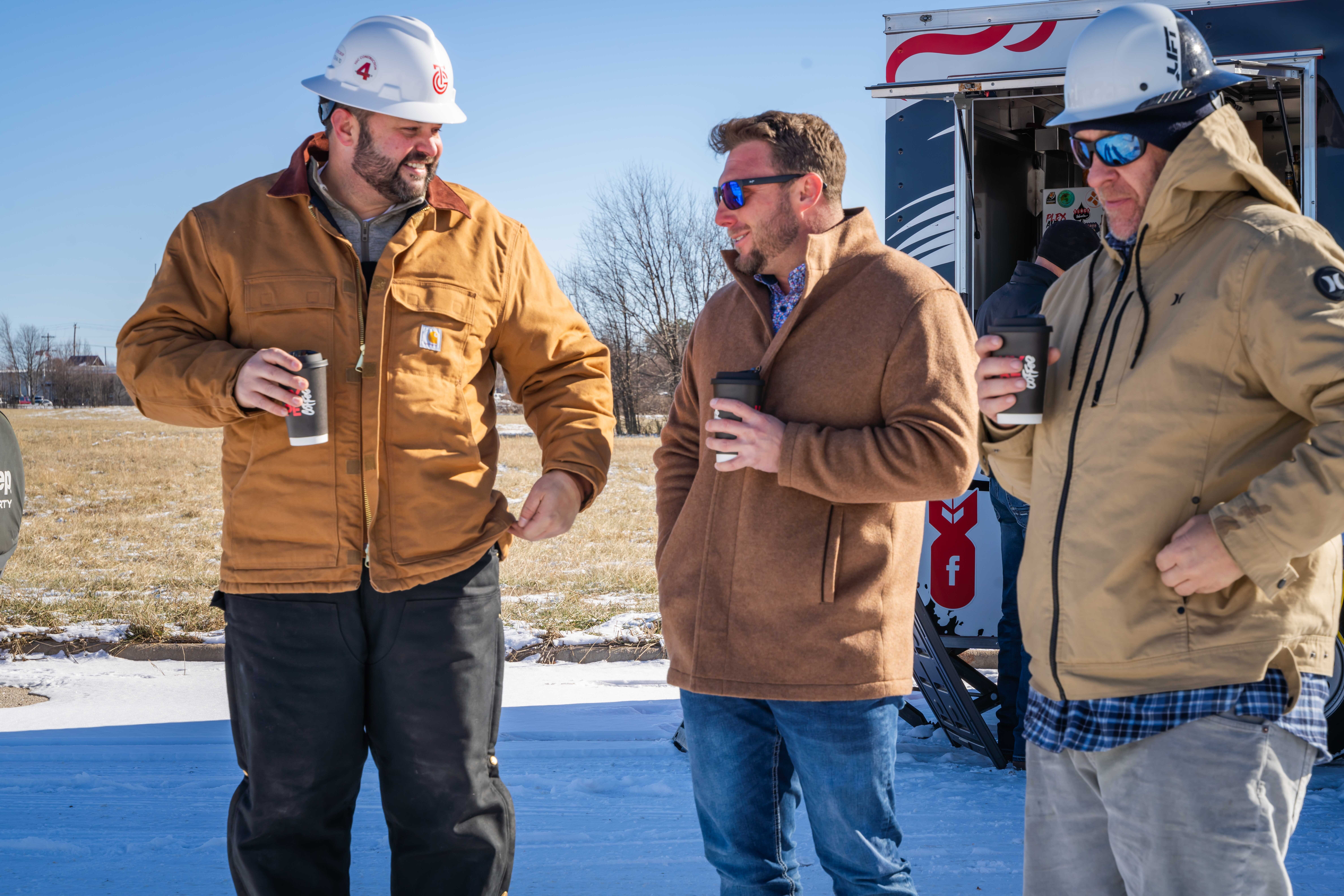 Three men talking and drinking coffee outside on a cold day