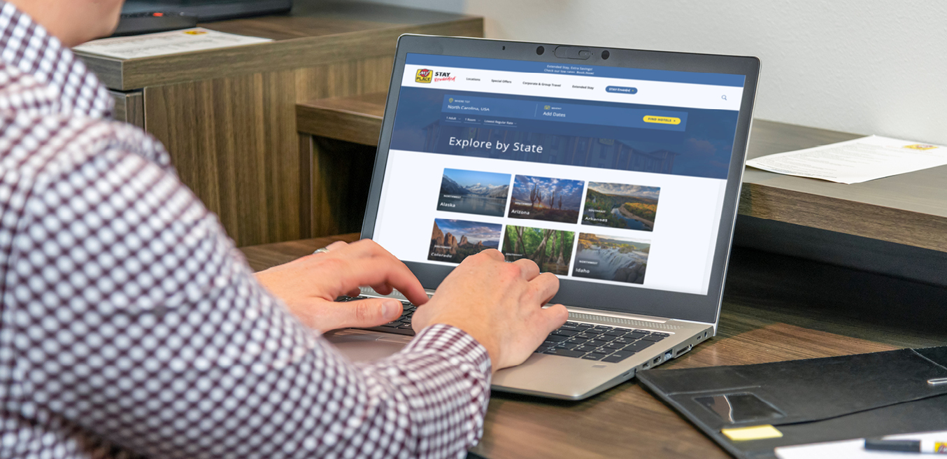 A man types on a laptop sitting on a My Place Hotel in-room desk.