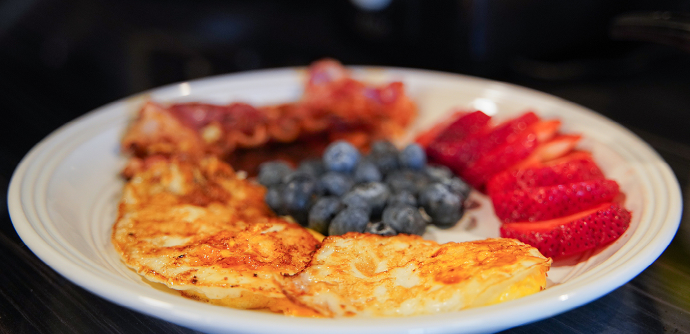 A plate of fried eggs, bacon, blueberries, and sliced strawberries.