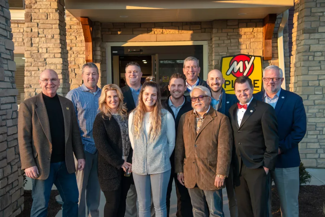 Eleven people smile and pose for the camera outside the hotel's front door in Plainfield, Indiana.