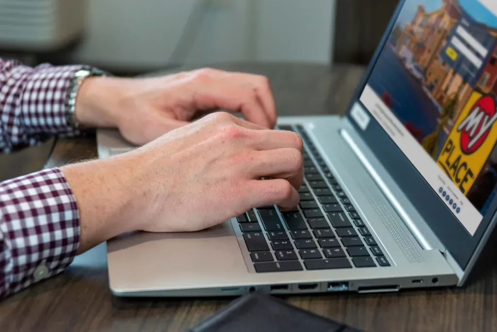 A man's hands type on a computer inside a My Place hotel room.