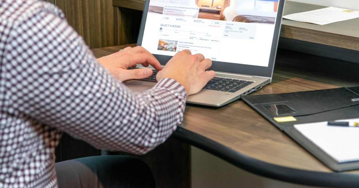 Man sitting at a desk inside a My Place Hotel room working on his laptop.