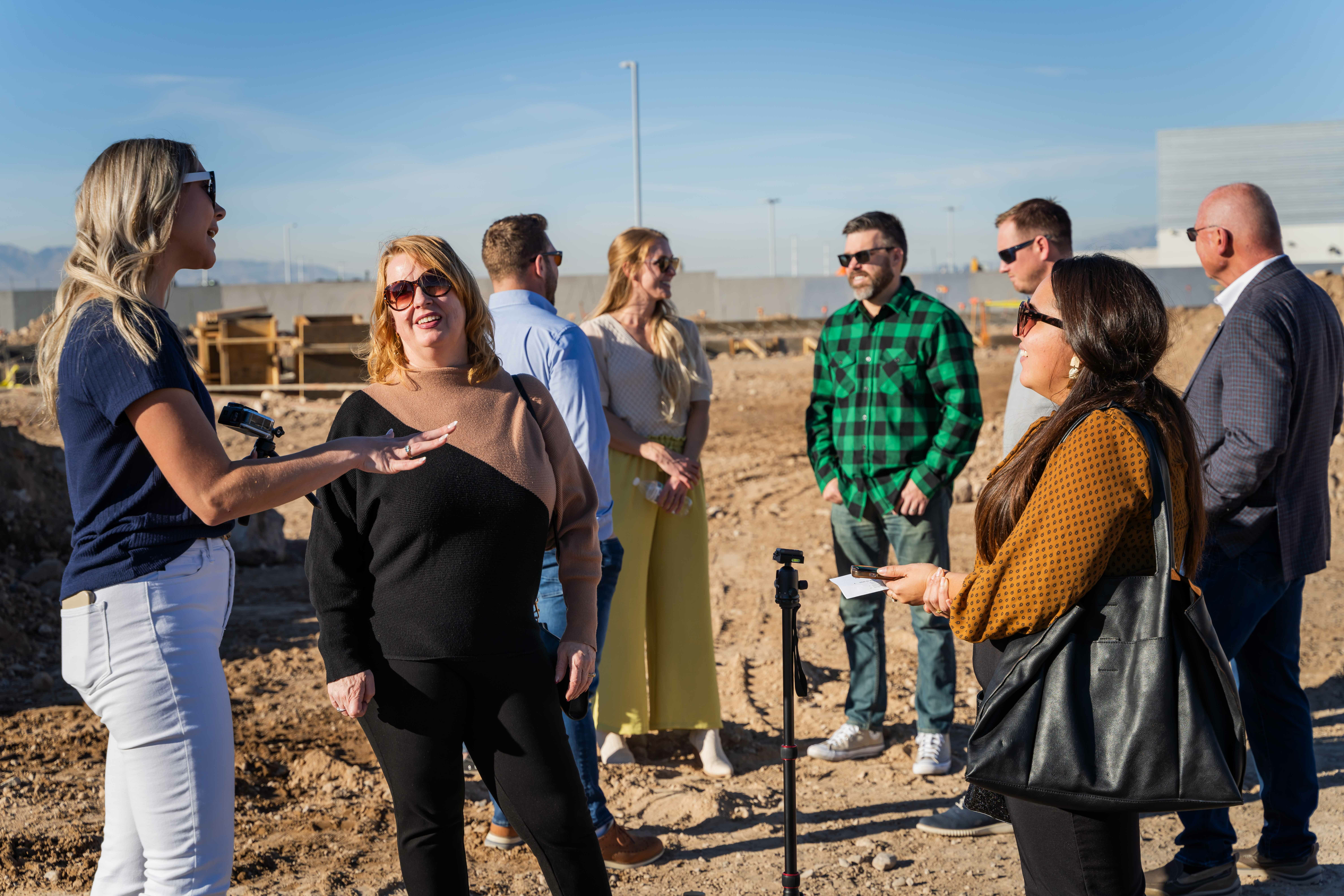 Three women talk in the foreground while five more people talk in the background at groundbreaking construction site.
