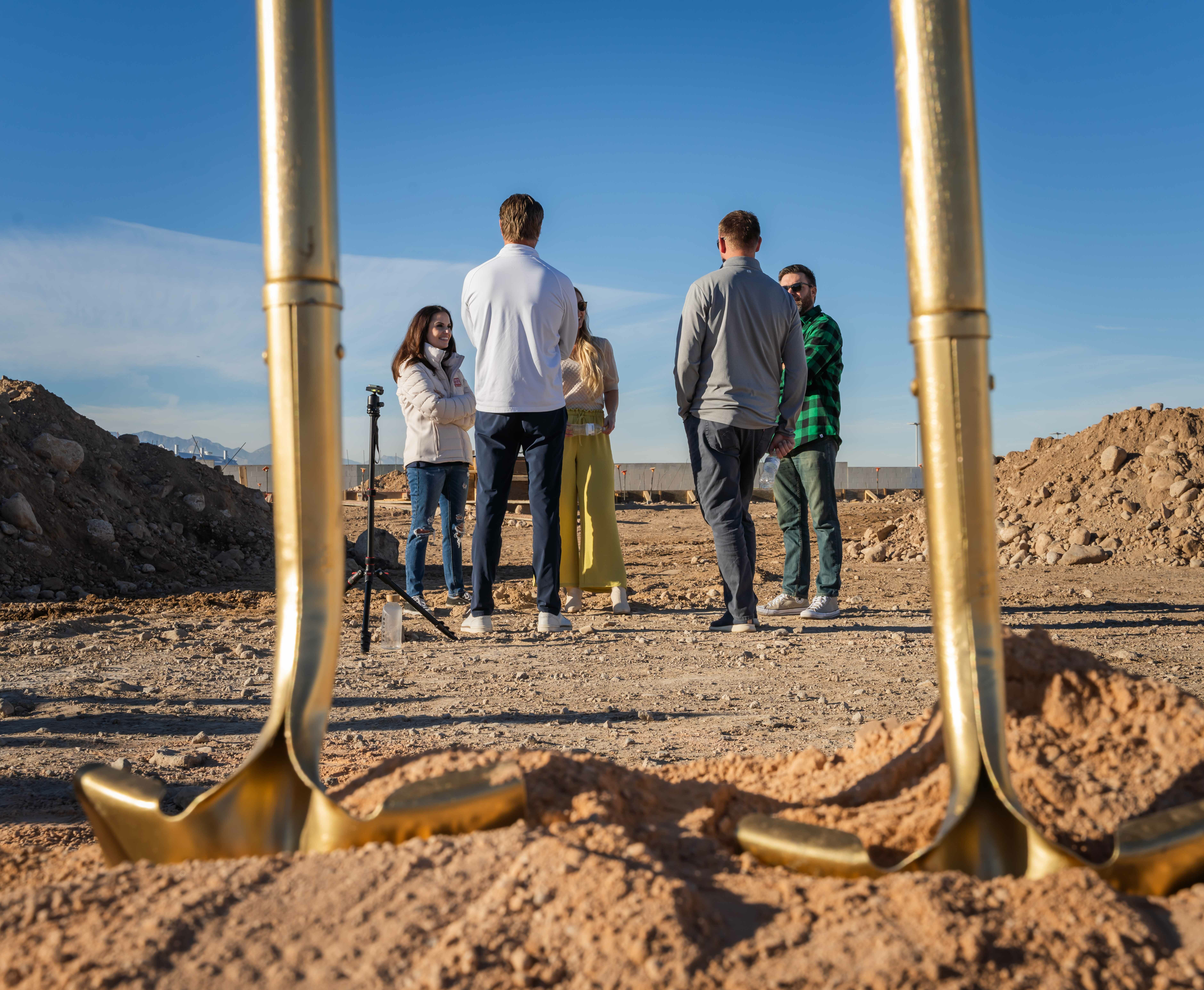 Two gold shovels in the foreground, group of five people in the background talking in a circle.