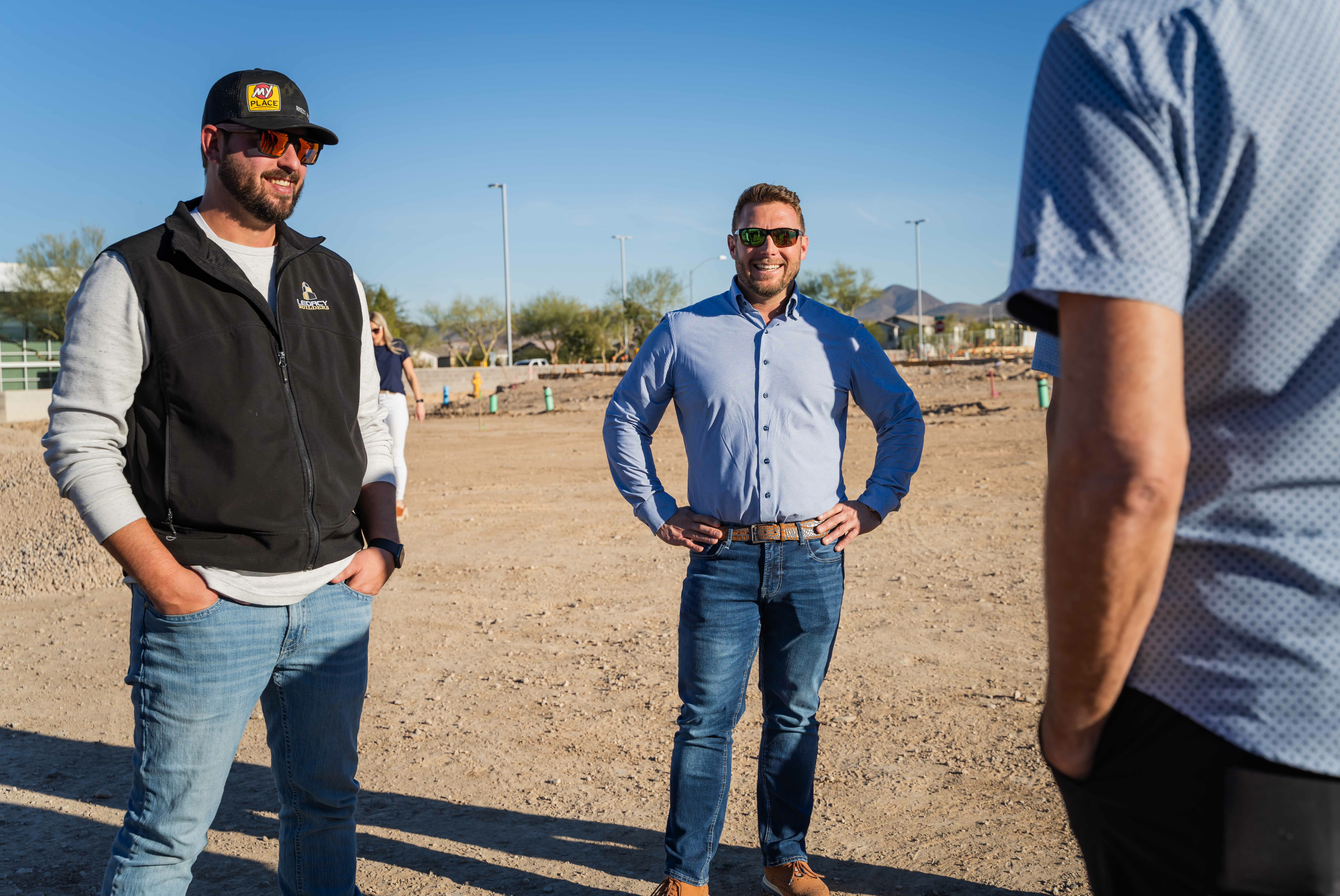 Three people standing in construction site during groundbreaking ceremony.