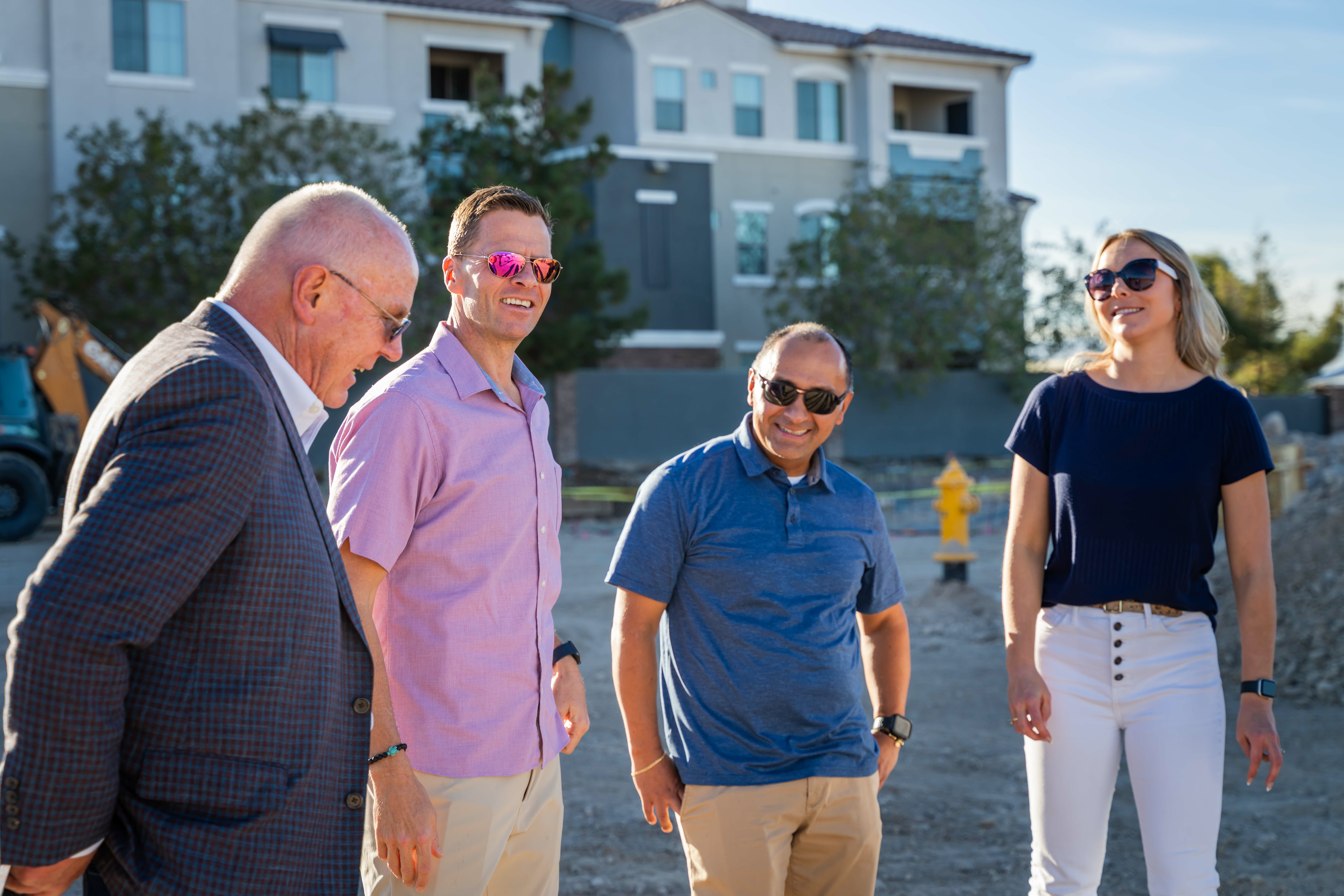 Four people standing and talking near groundbreaking site.