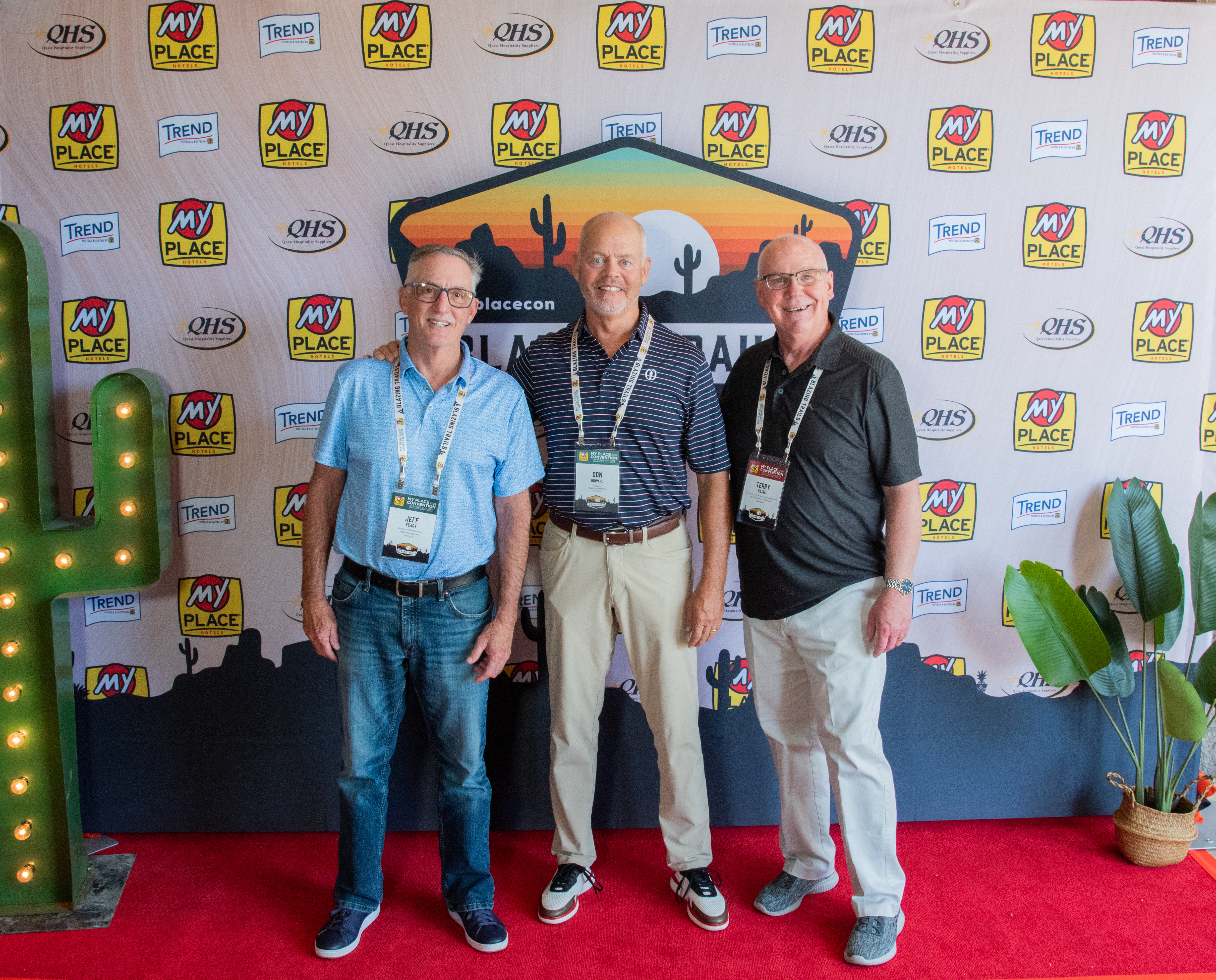 Three men posing in front of a backdrop at a hospitality conference