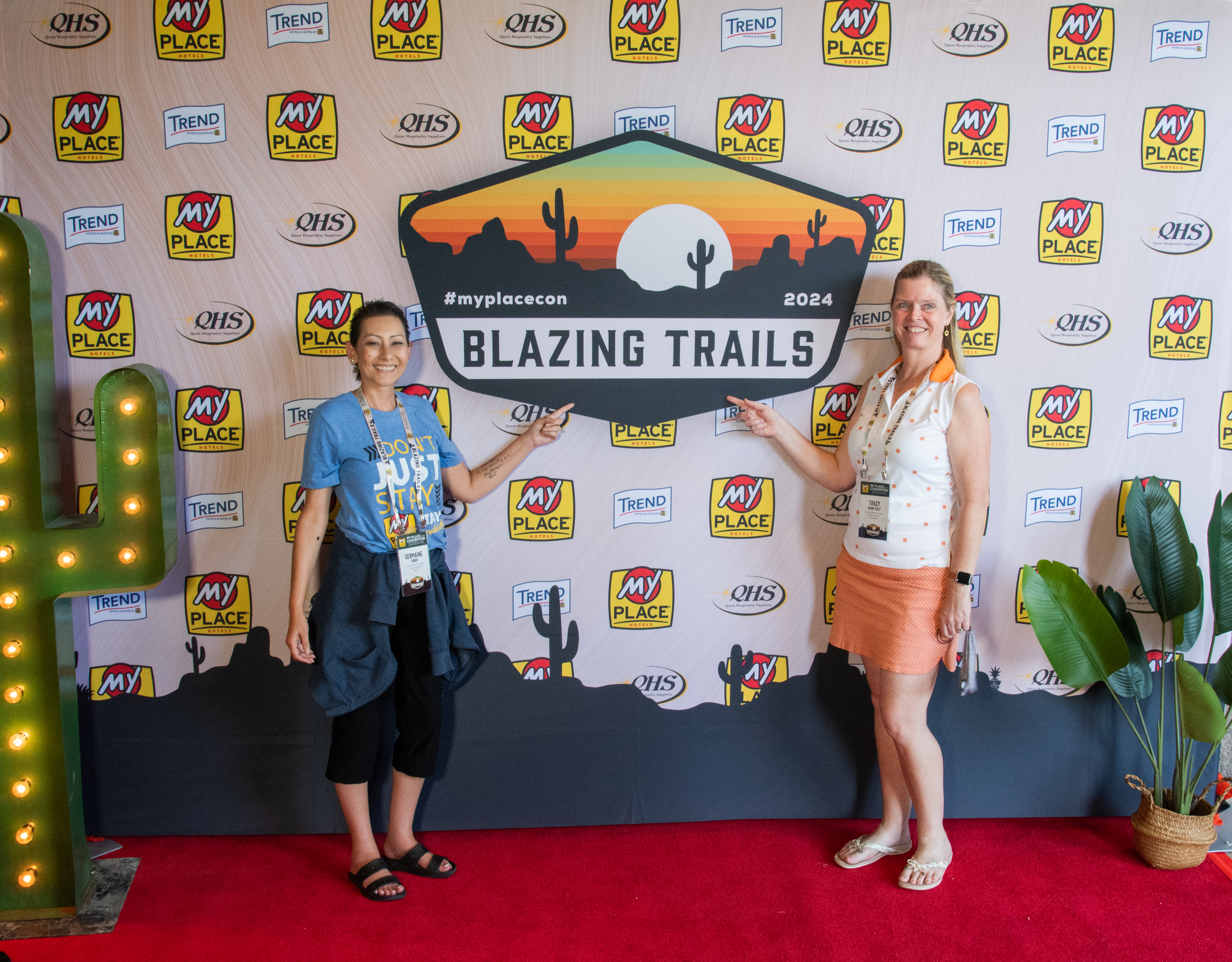 Two women posing in front of a backdrop at a hospitality conference