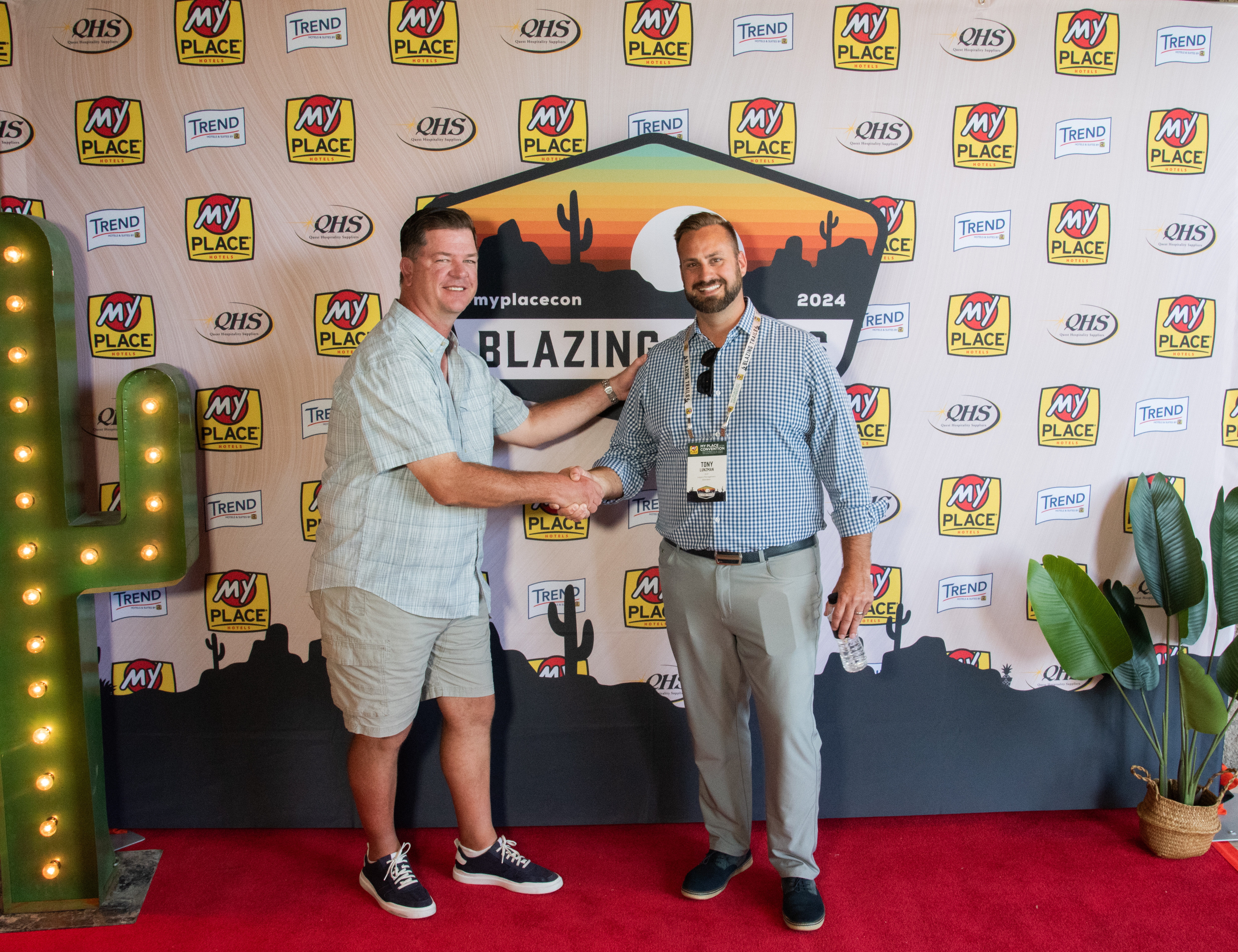Two men posing in front of a backdrop at a hospitality conference