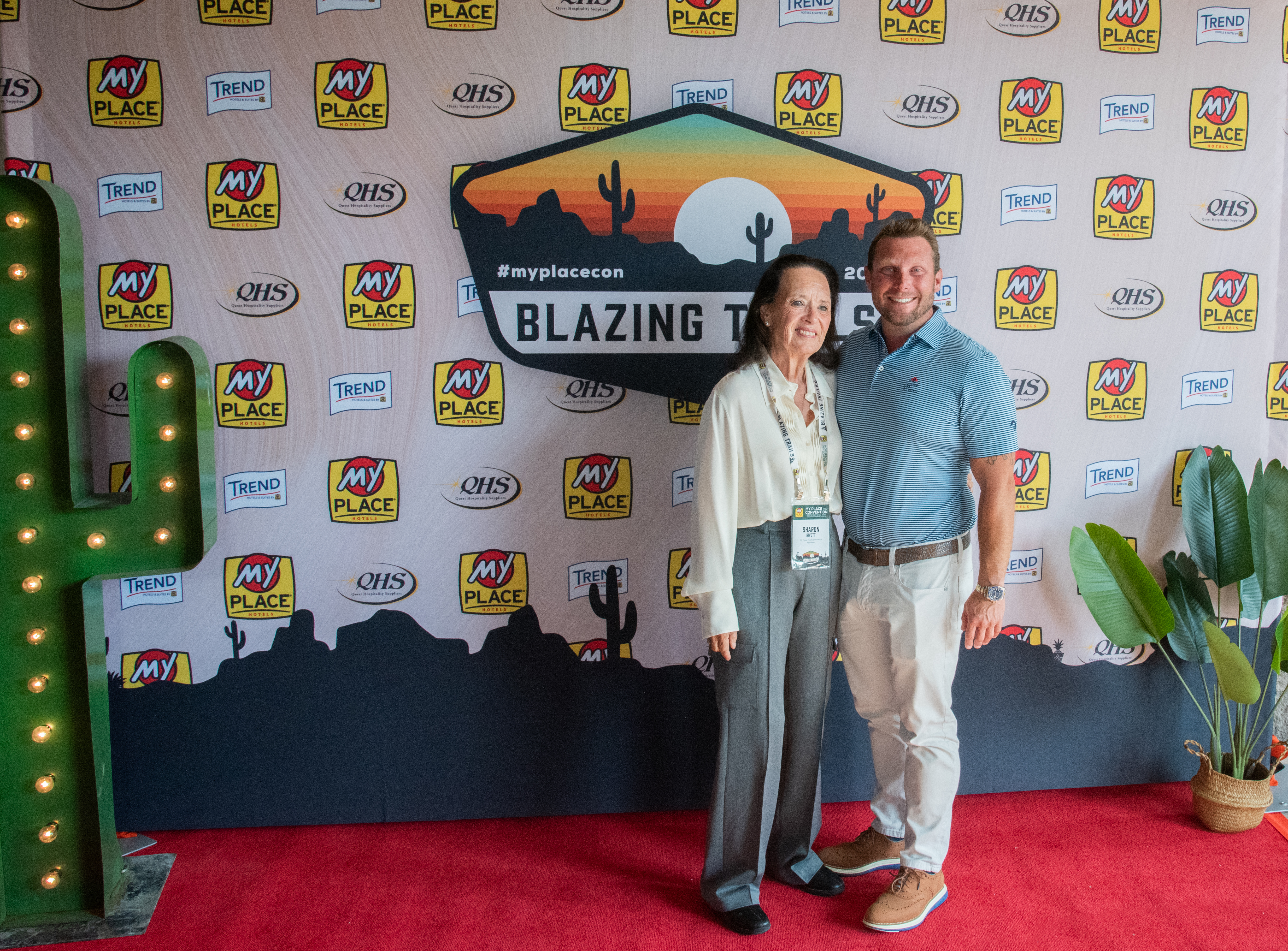 Two individuals posing in front of a backdrop at a hospitality conference