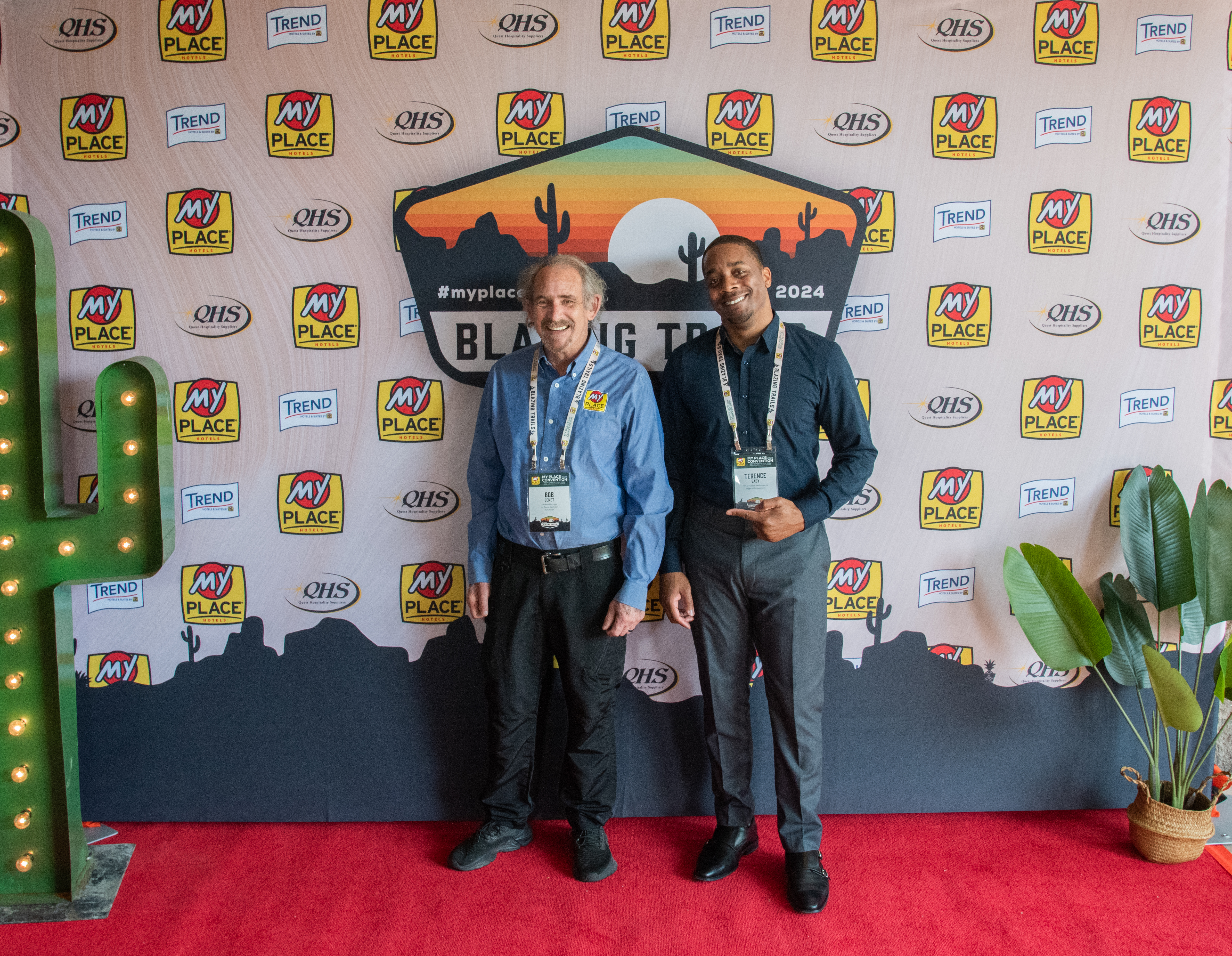 Two men posing in front of a backdrop at a hospitality conference