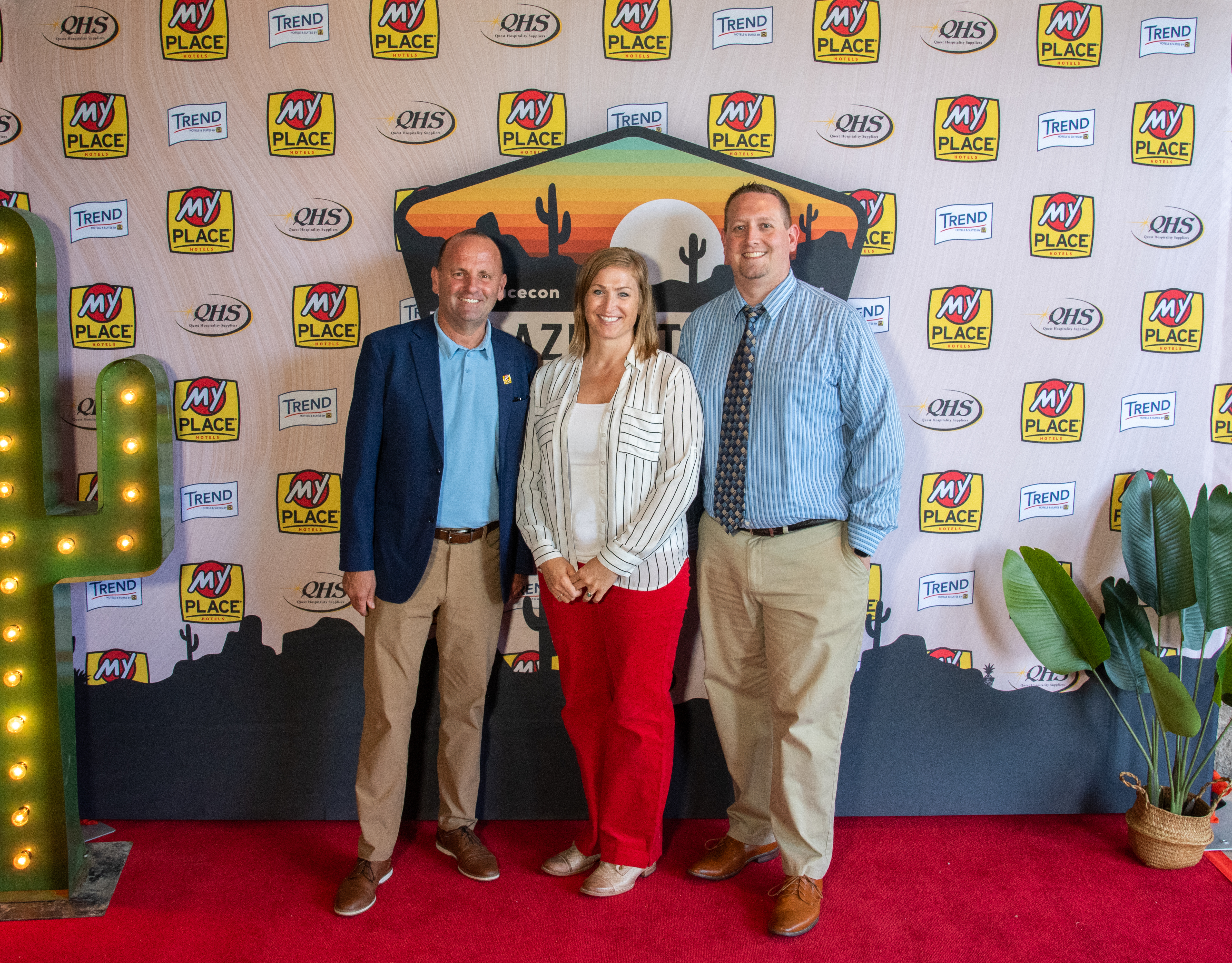 Three people posing in front of a backdrop at a hospitality conference
