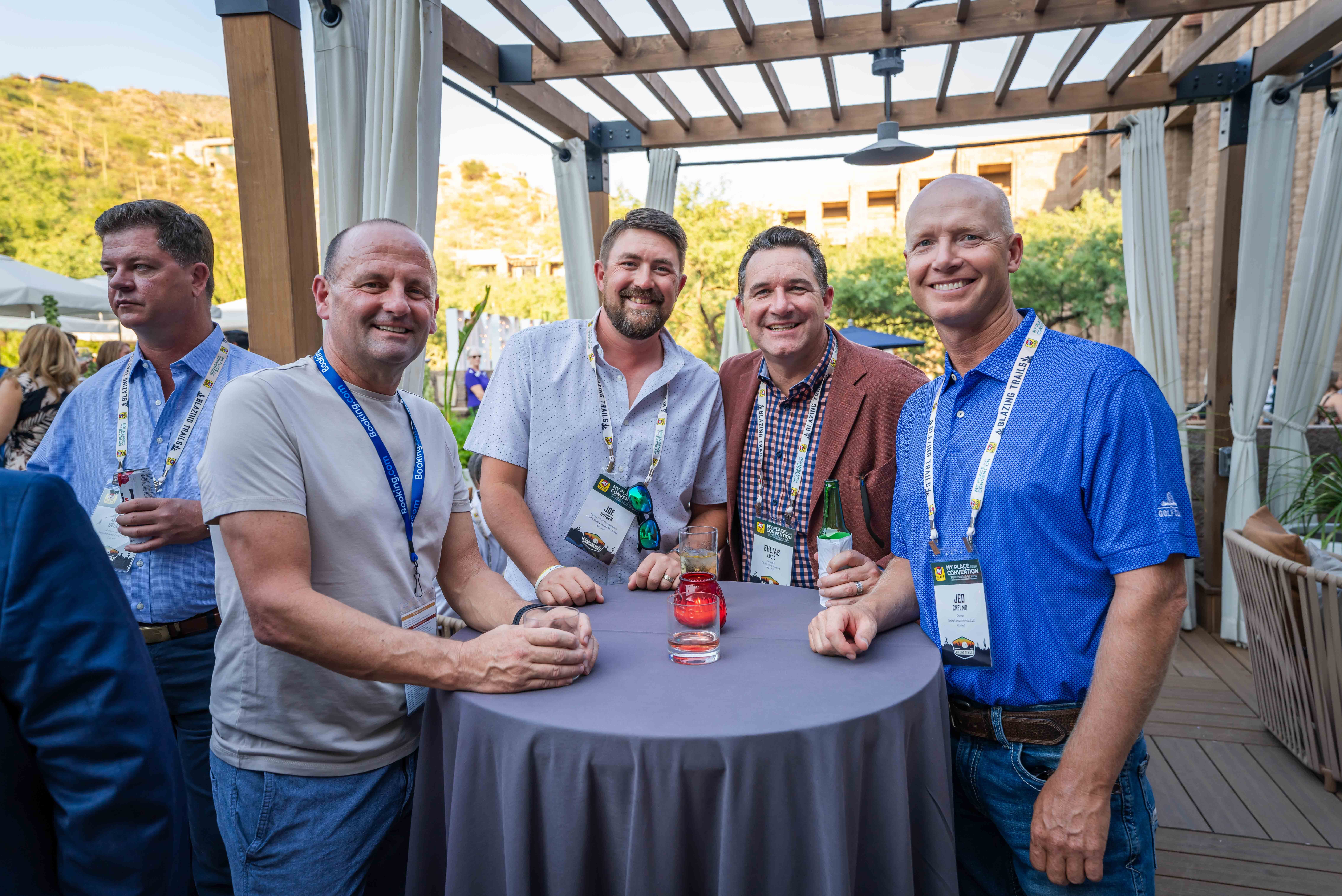 A group of four men smiling for the camera at an outdoor cocktail hour