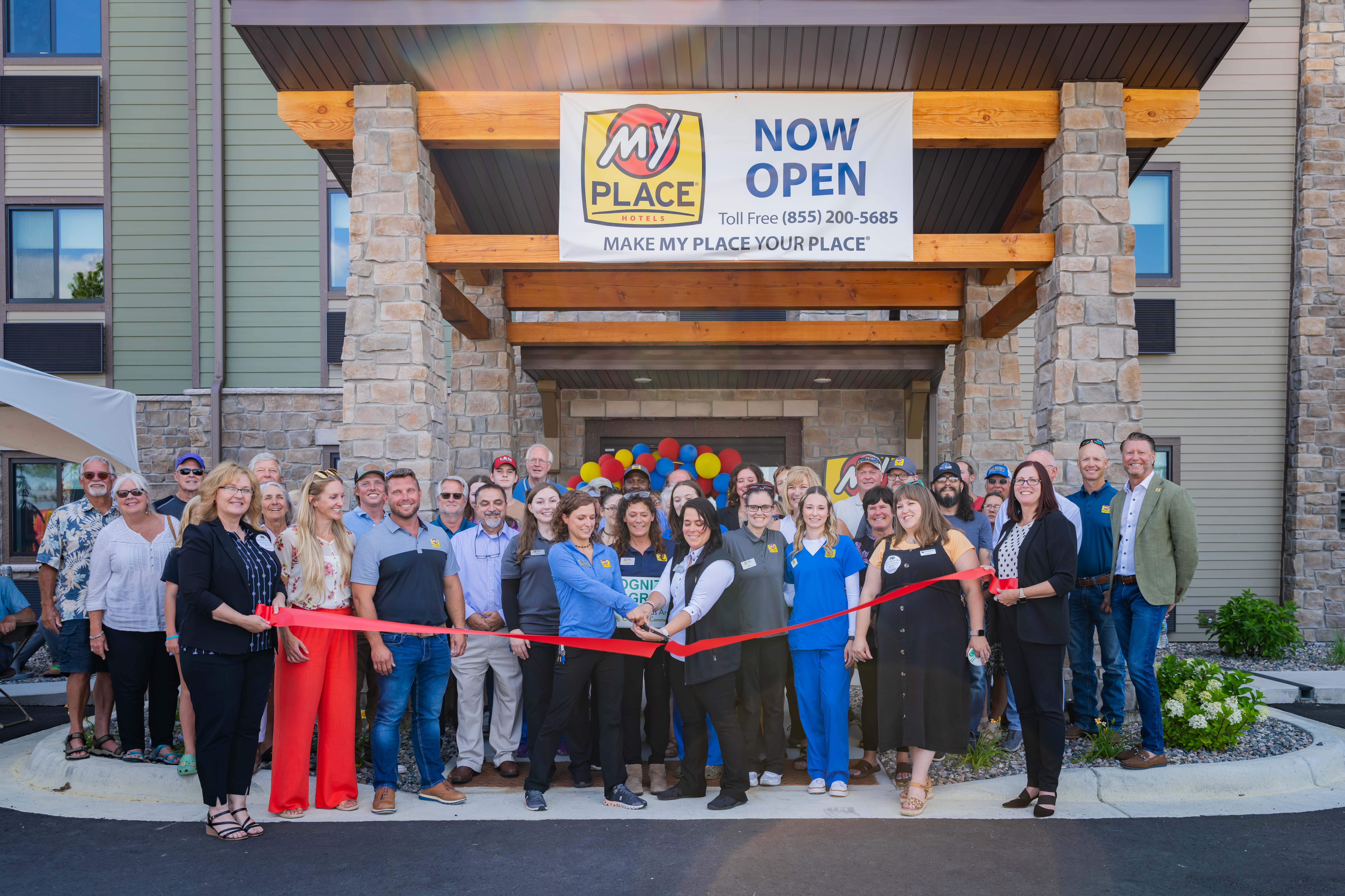 A group of people posing for a riboon cutting ceremony outside of a hotel.