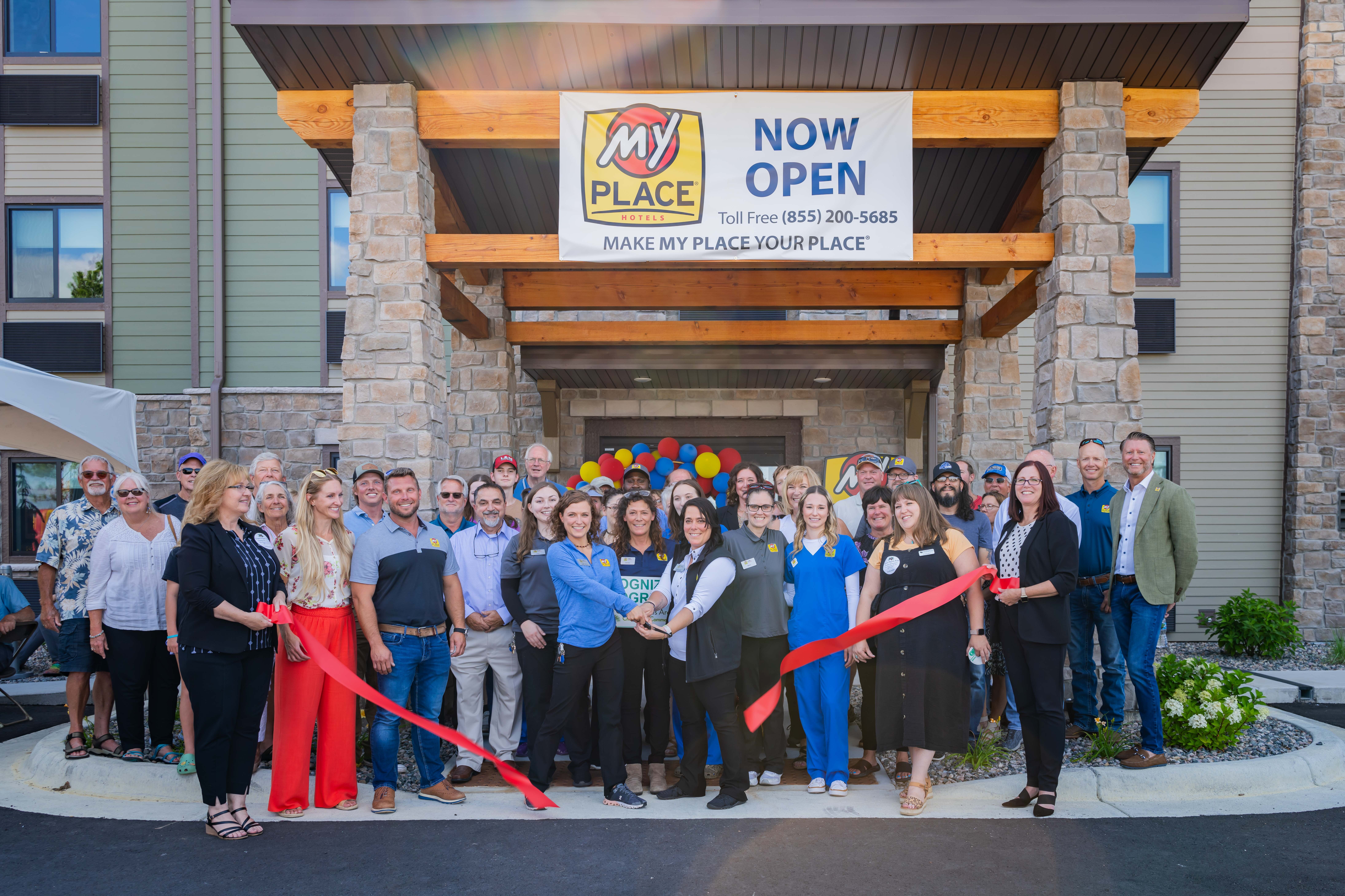A group of people performing a ribbon cutting ceremony outside a hotel