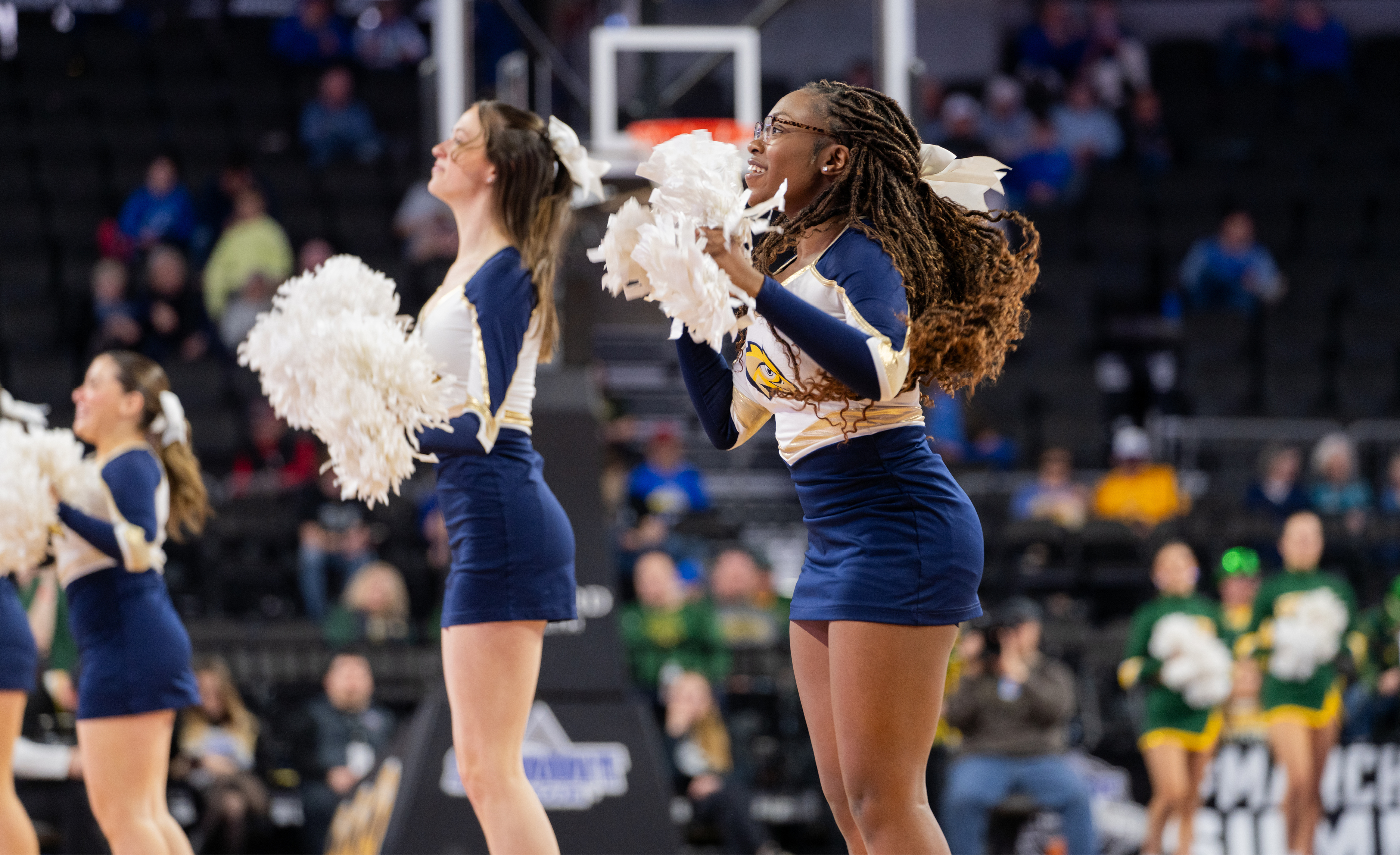 Two cheerleaders wearing navy blue and white lead a cheer to an off-camera crowd.