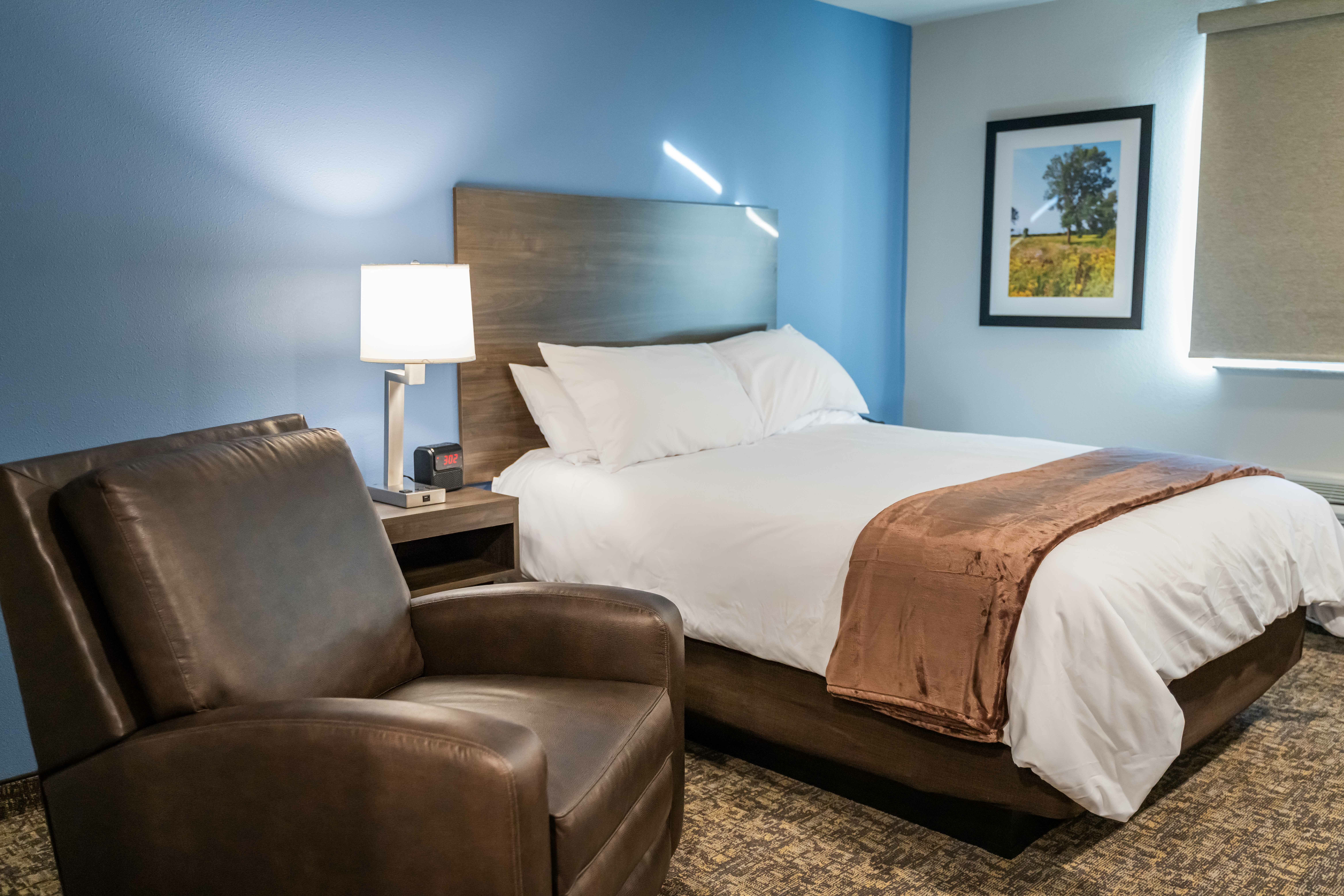 Interior of hotel room showing blue walls, brown recliner and queen size bed.