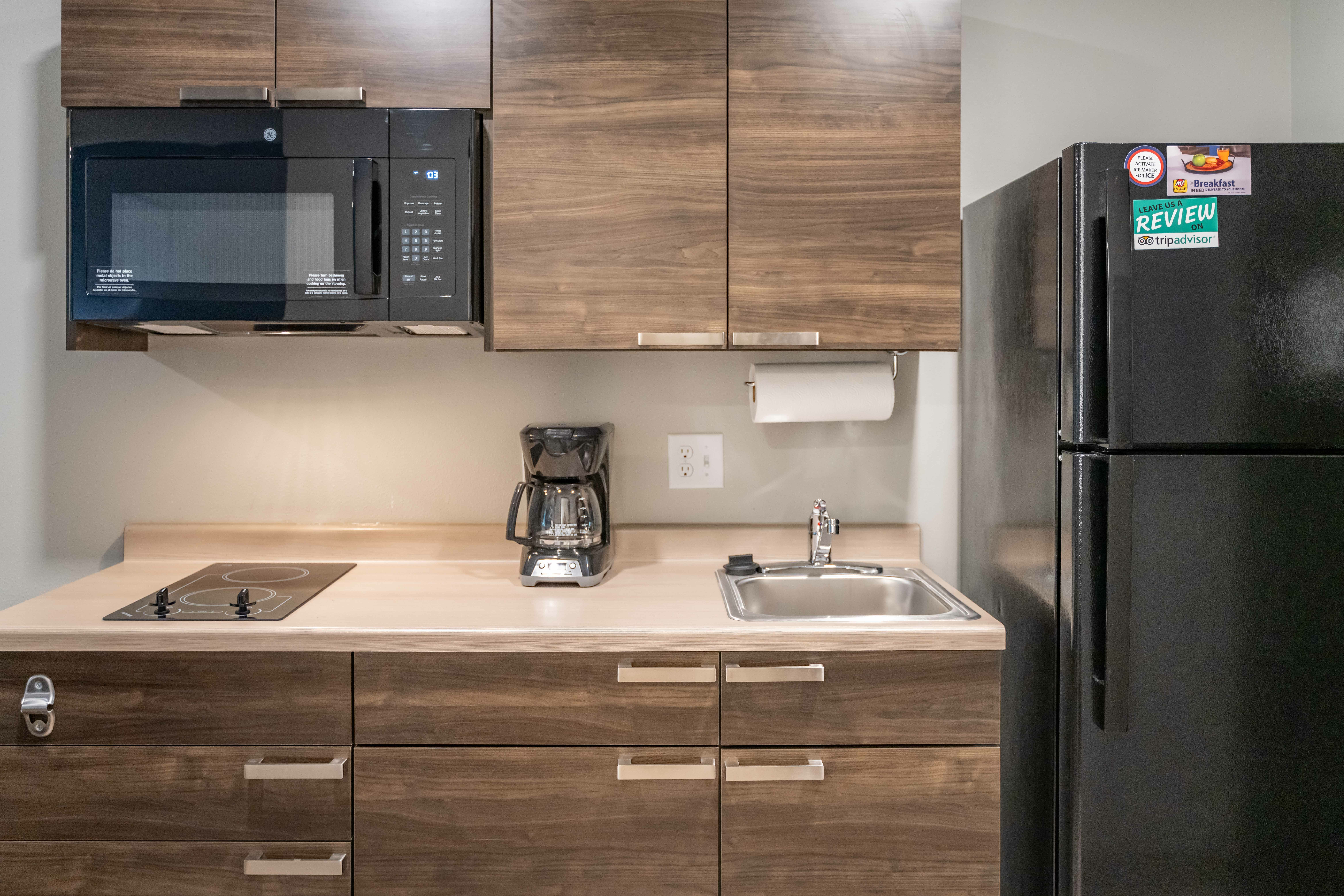Interior of hotel room directly facing kitchenette, with cupboards and microwave on the left and fridge on the right.