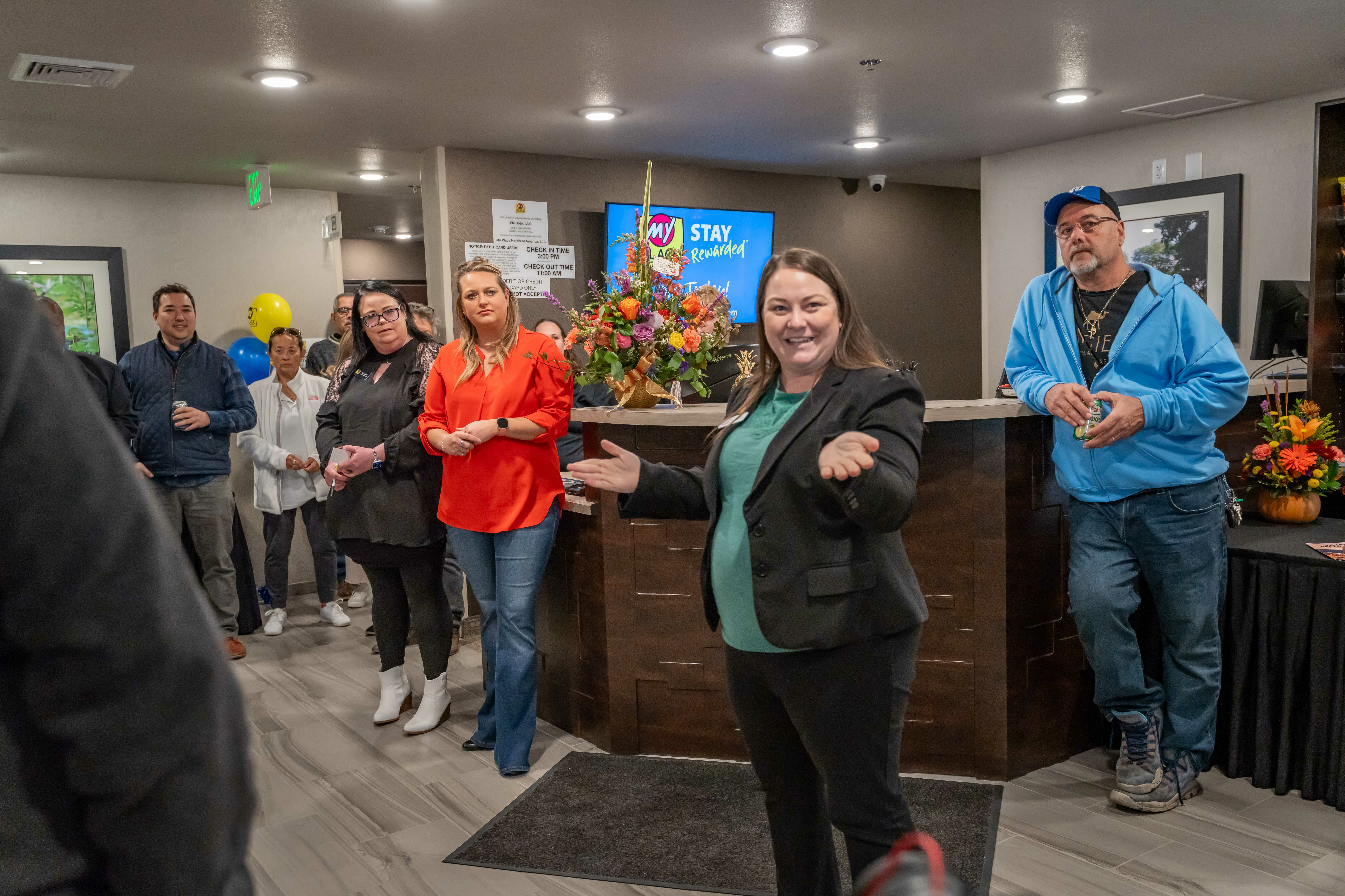 A woman smiles while addressing a small crowd near the front desk during the hotel's grand opening celebration.