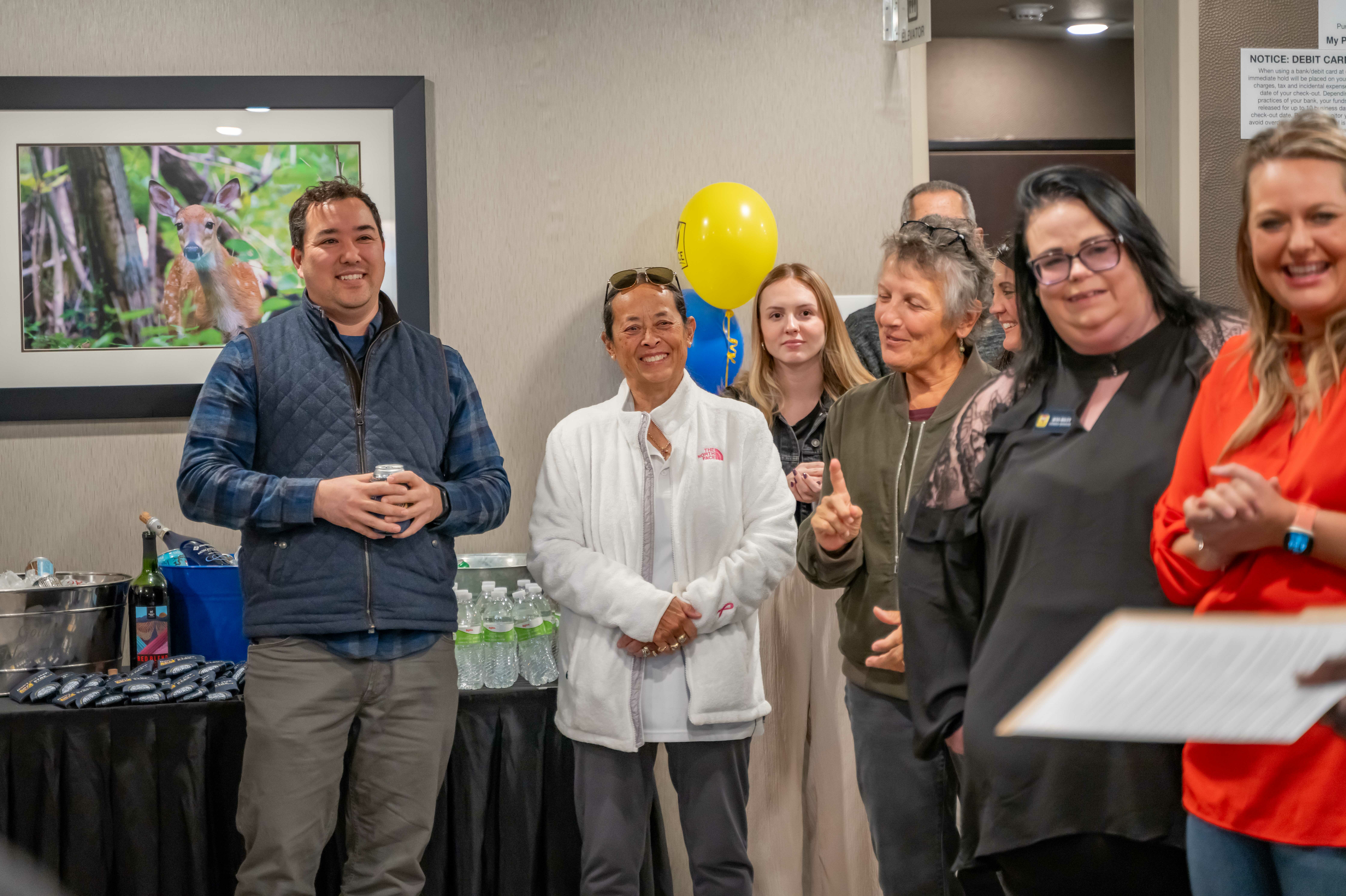 A group of spectators smile at an on-camera speaker in the lobby during the hotel's grand opening celebration.