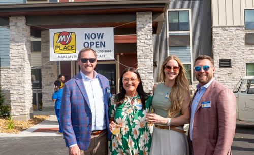 Four professionals are posing for a picture, standing outside of the new My Place hotel.