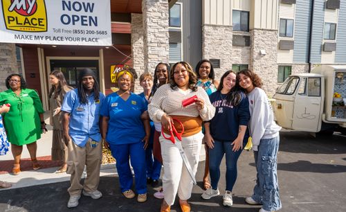 Professionals are pictured standing in front of the "Now Open" sign with the giant scissors used to cut the ribbion.