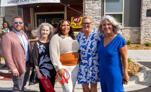 Five professionals are pictured posing in front of the "Now Open" sign, hung above the doors of the new hotel.
