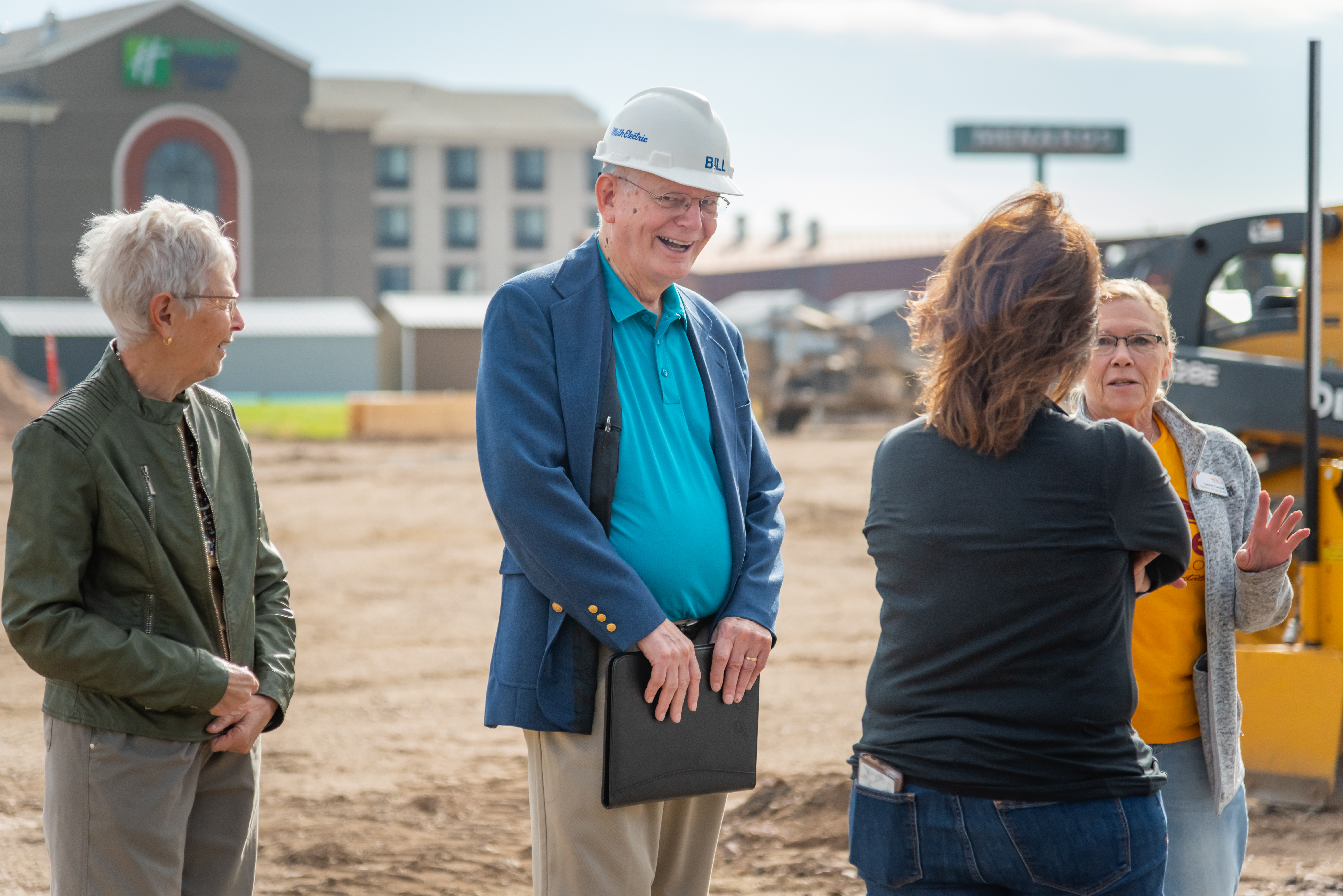A man smiles and laughs while talking to three women at a groundbreaking site in Mitchell, SD.