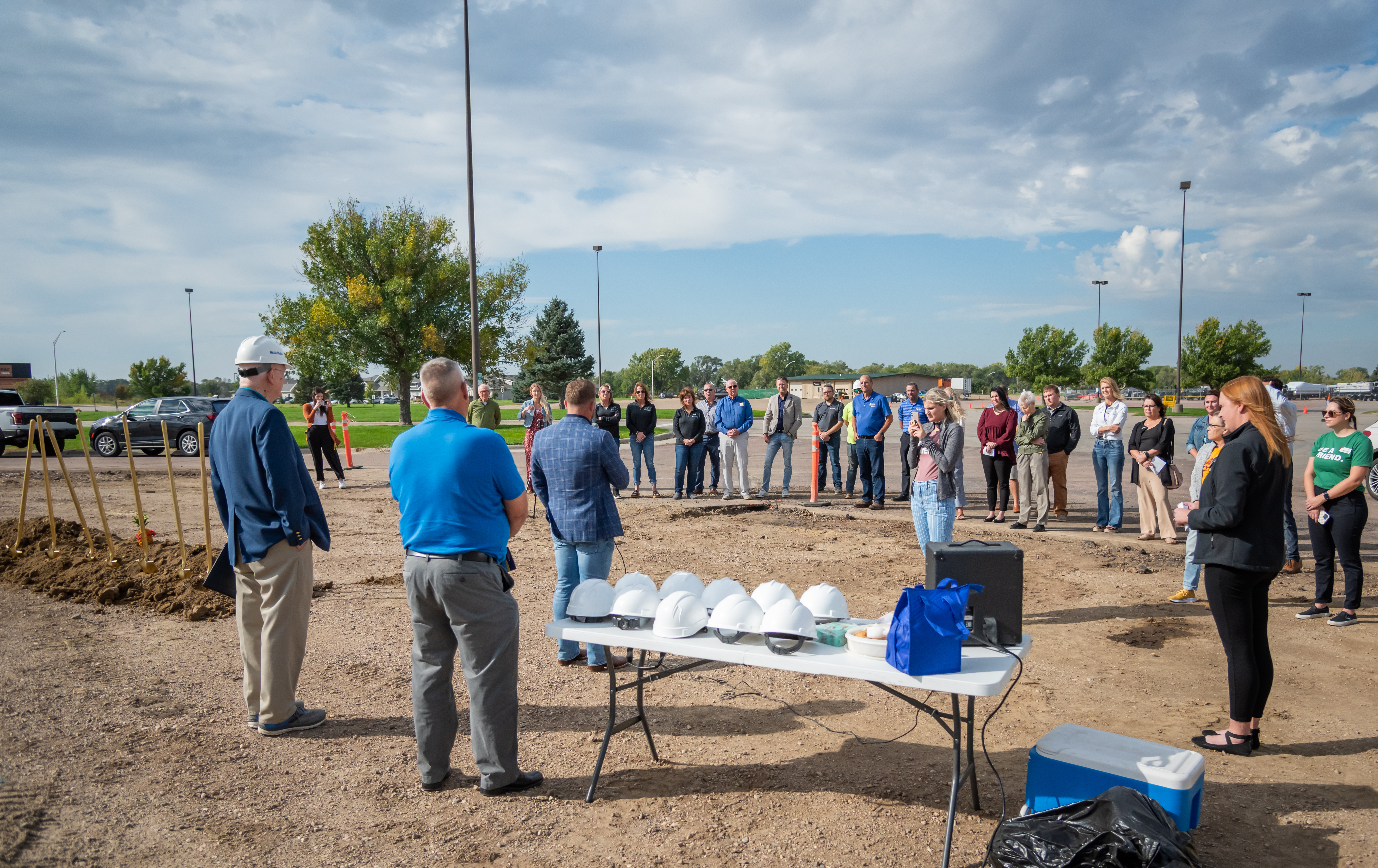Wide shot of a man addressing a crowd of about 30 people under a cloudy sky.