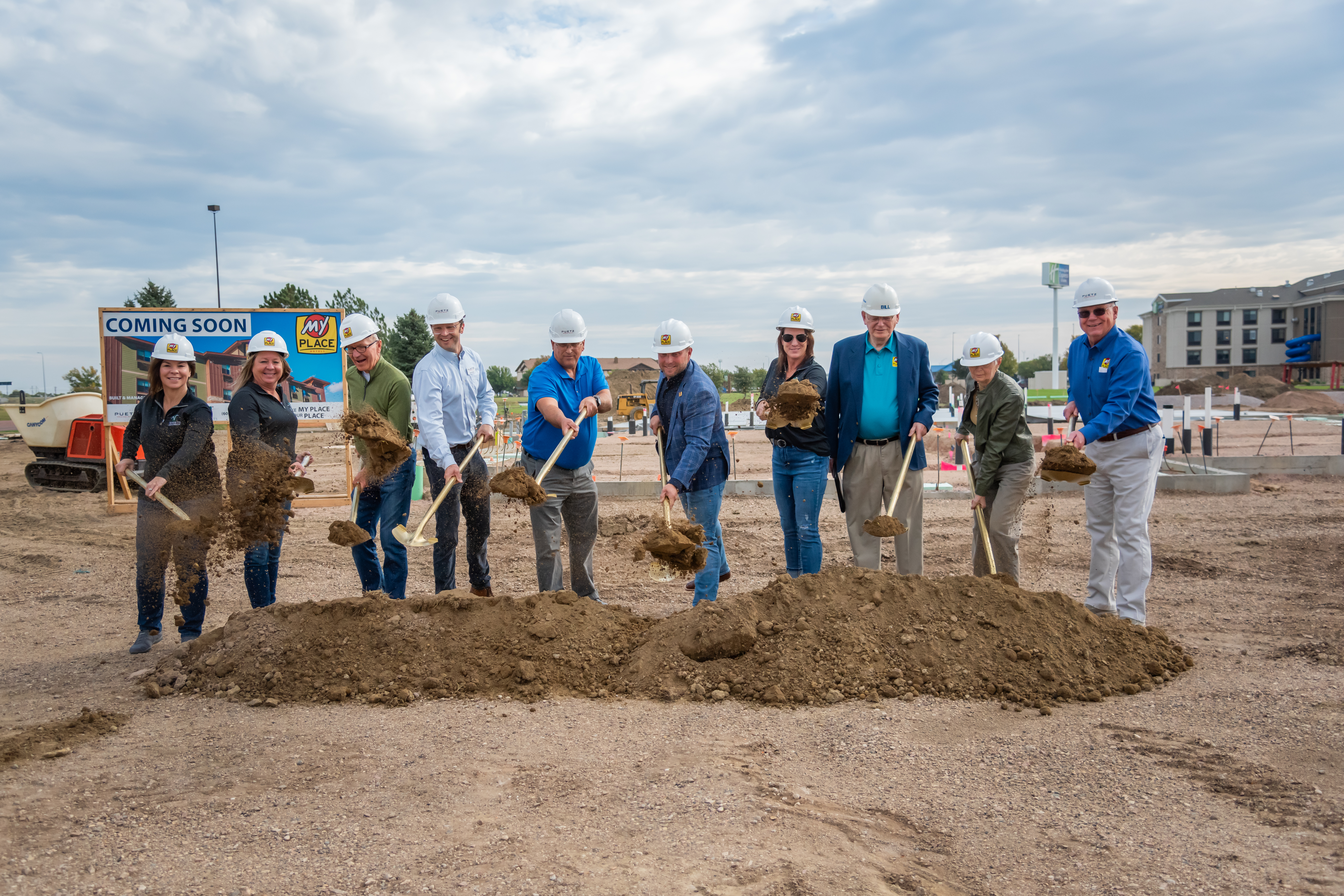 Ten people hold shovels and scoop dirt at a groundbreaking site in Mitchell, SD.