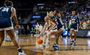 A woman in a white jersey dribbles a basketball while a woman in a navy blue jersey defends her.