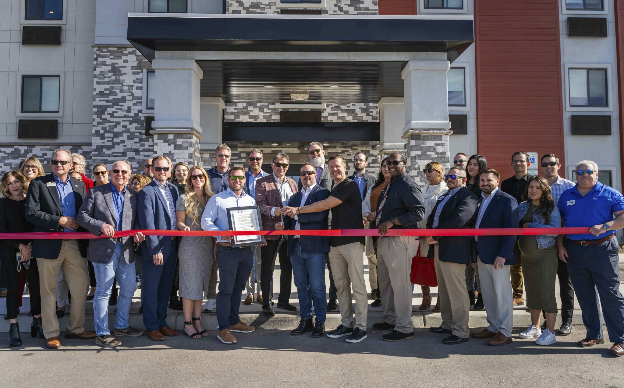 A crowd of people pose outside the hotel entrance ahead of cutting a red ribbon during the grand opening celebration in Nampa, Idaho.