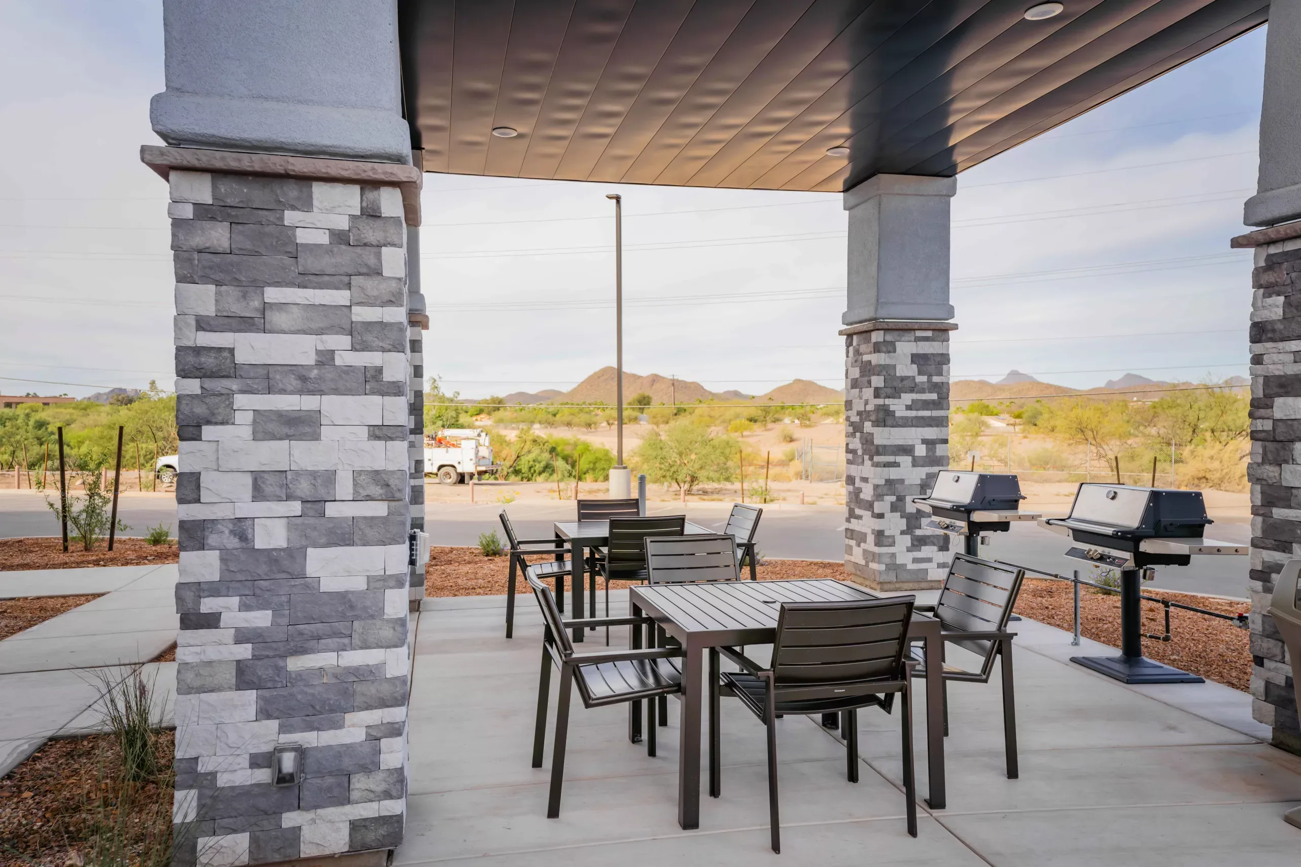 A paved patio under a stone pavilion with tables, chairs and two grills.
