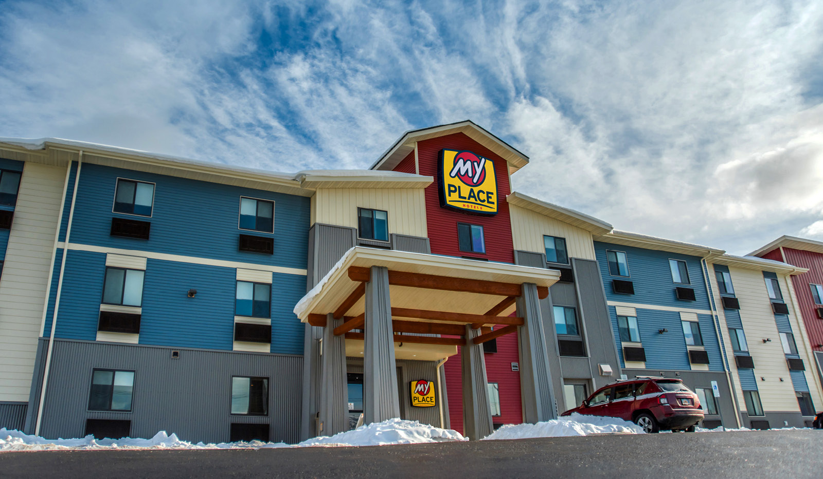 Front entrance of My Place Hotel-Ketchikan with snow on the ground and wispy clouds in the sky.