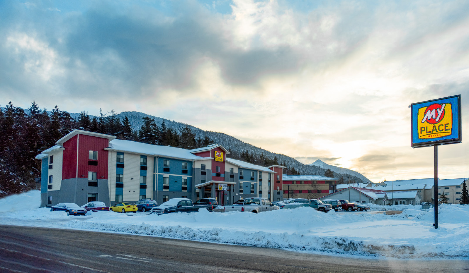 Street view of My Place Hotel with the logo sign, mountains and evergreens in background.
