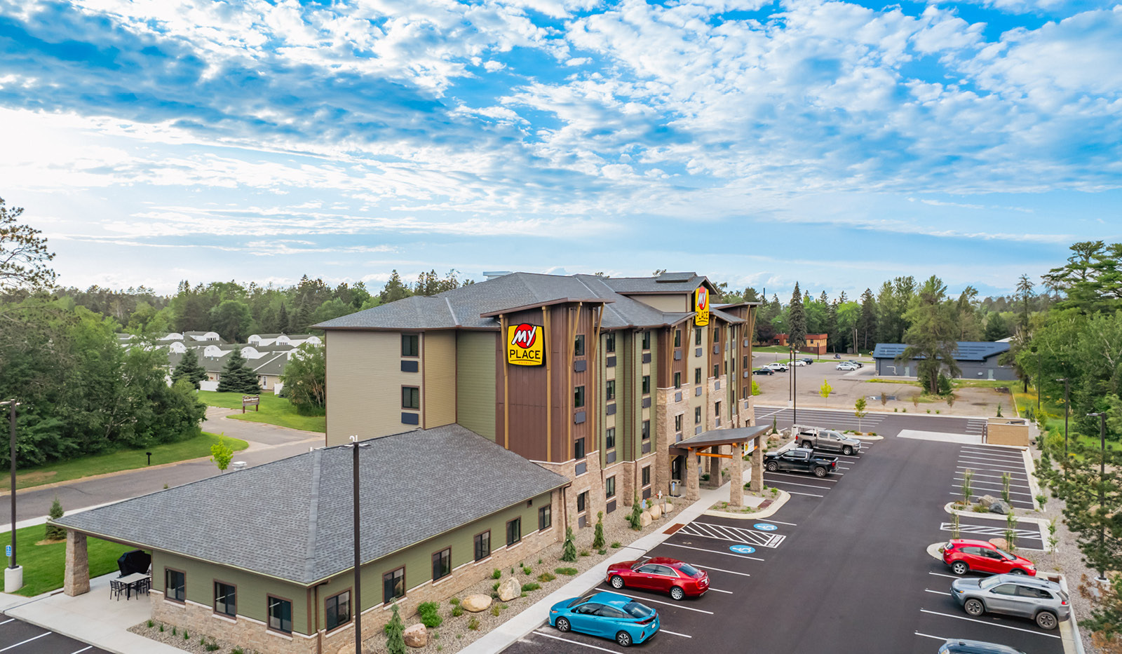 Exterior side view of hotel highlighting the indoor pool. Light blue sky with fluffy clouds highlight the dark green building.