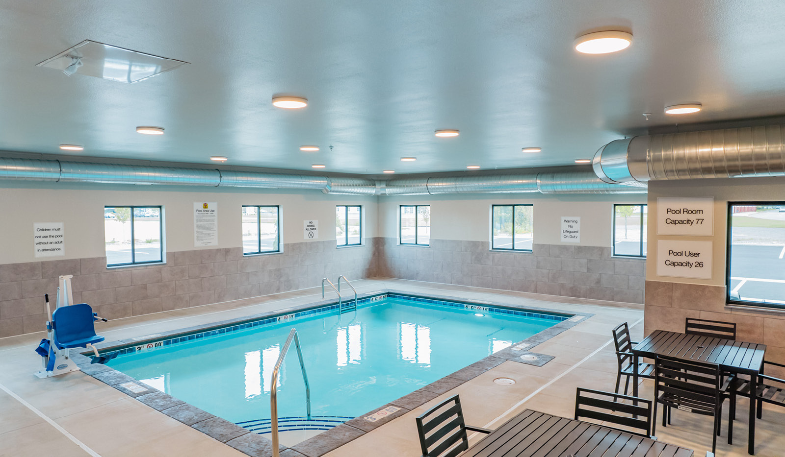 Indoor pool with accessibility access chair for the pool. Indoor area also includes tables and chairs.