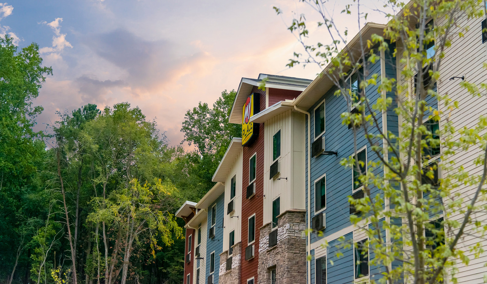 Exterior of My Place Hotel-Huntersville, NC with tall green trees surrounding the side of the property.