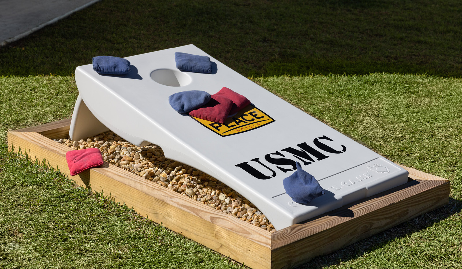 Bean bag game board in grass with blue and red bean bags scattered on the board.