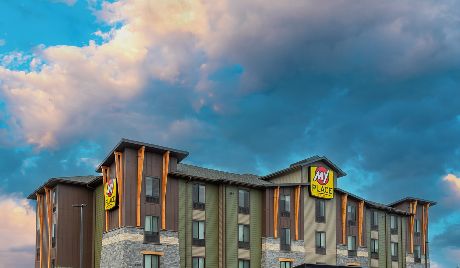 Top half of exterior of My Place Hotel-Portland East, OR showing logo sign and a cloudy sky.
