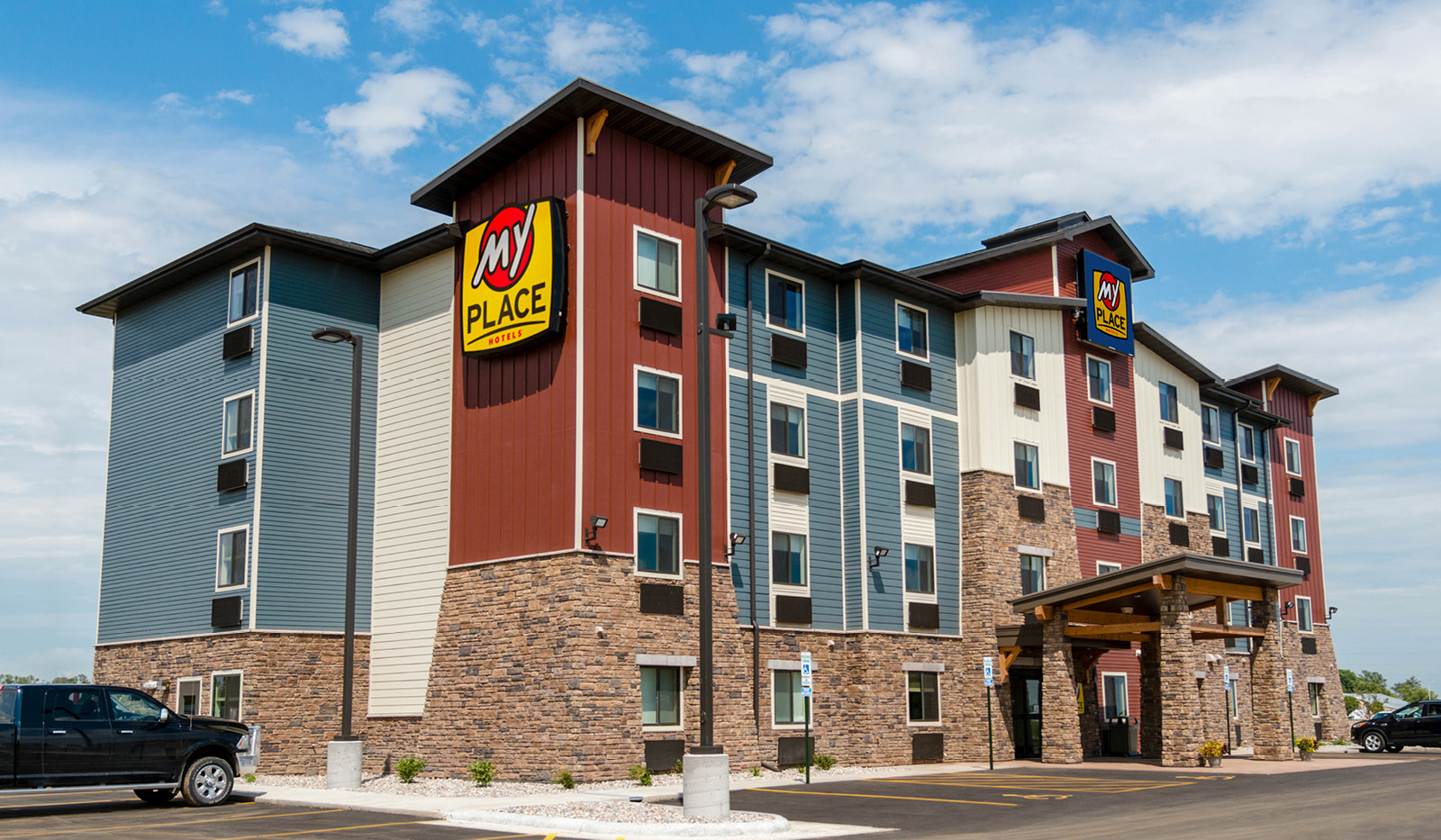 Exterior of My Place Hotel-Brookings, SD under partly cloudy blue sky.