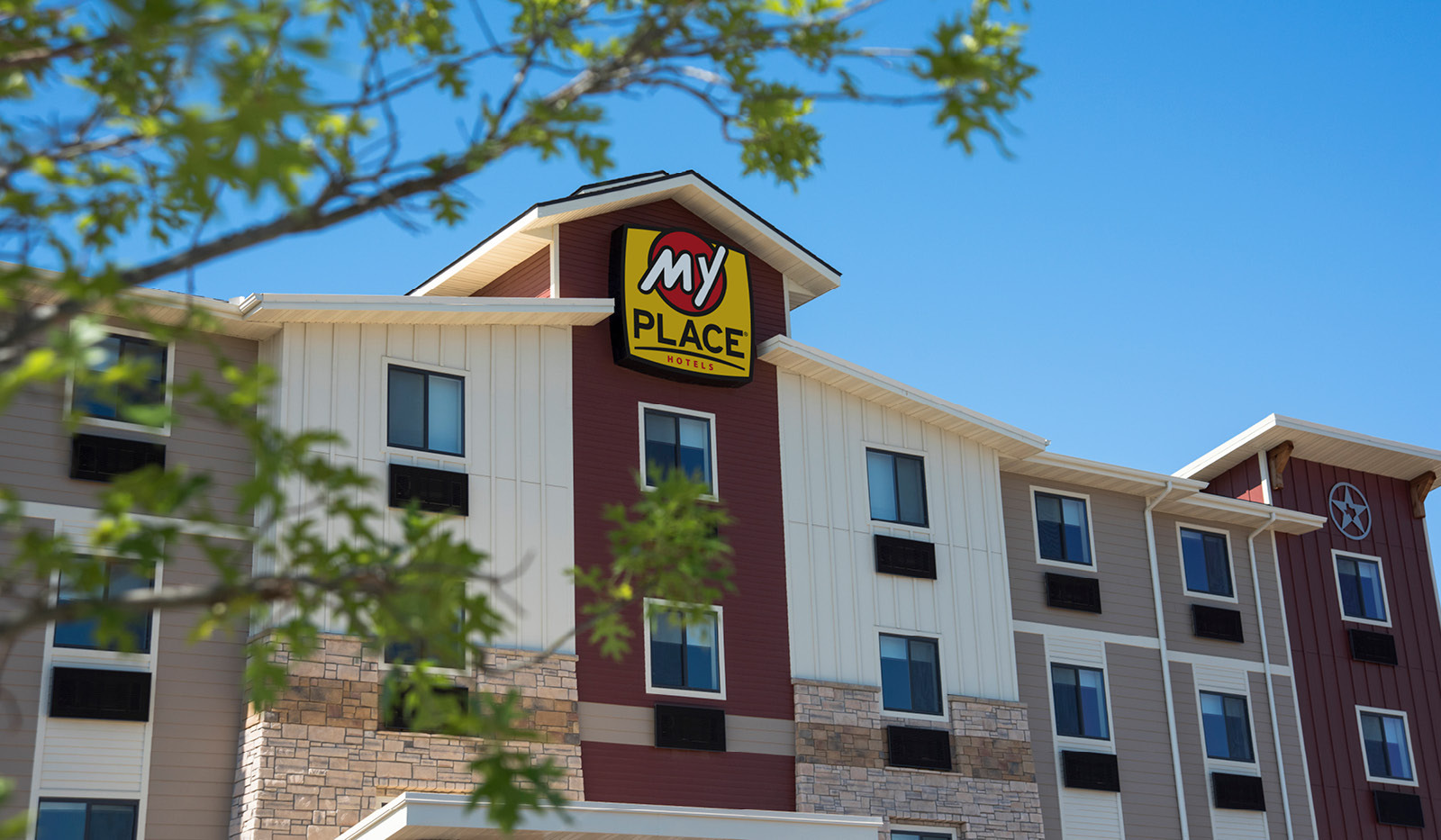 Exterior of My Place Hotel-Amarillo, TX seen through the branches of a tree.
