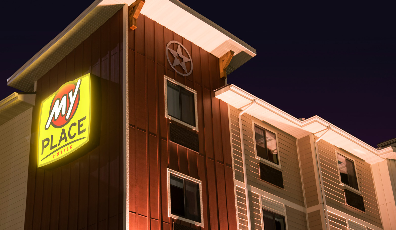 Close angled exterior of My Place Hotel-Amarillo, TX showing illuminated logo sign at night.