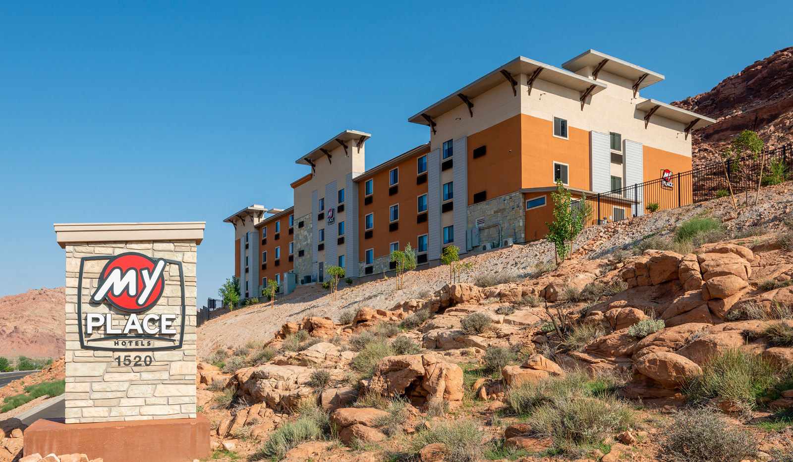 Wide exterior My Place Hotel-Moab, UT with logo sign under a clear blue sky.